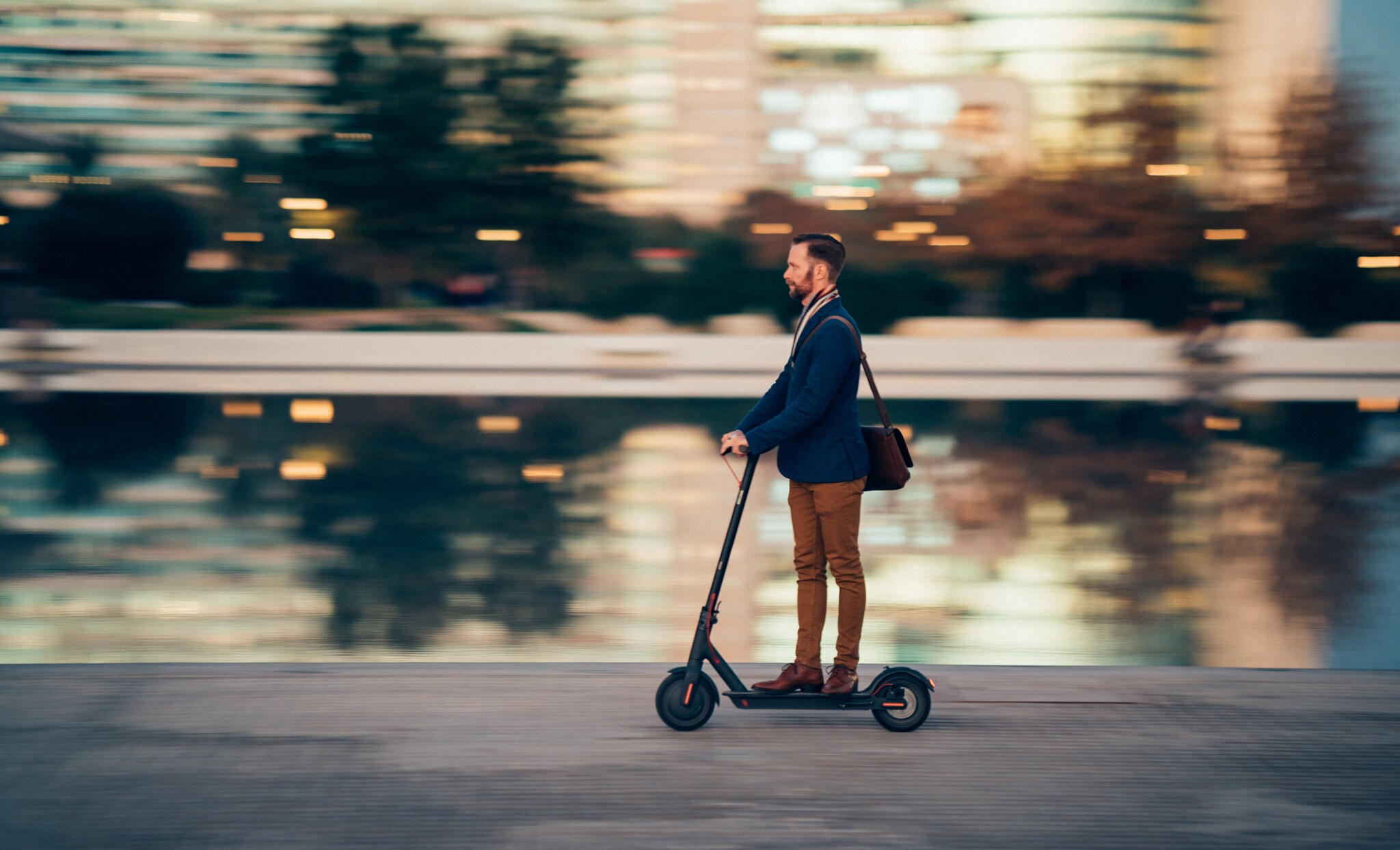 Profilansicht eines Geschäftsmannes, der auf dem Weg zur Arbeit einen Roller fährt