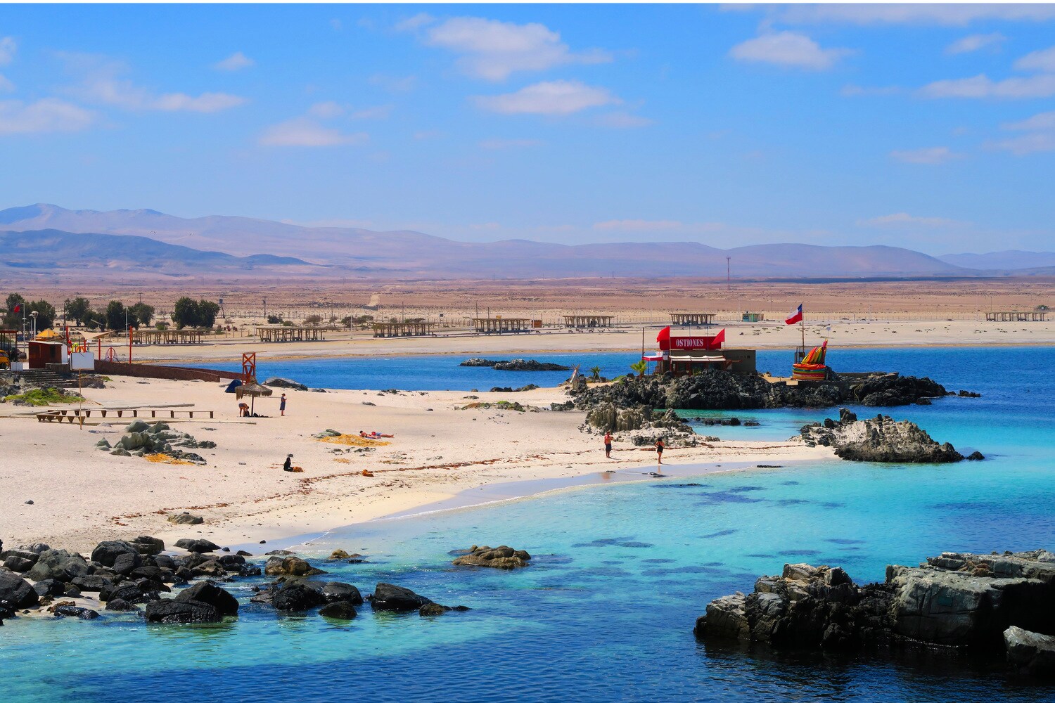 Eine Bucht in einem Urlaubsort mit Sandstrand und flachen Felsformationen Eine Bucht in einem Urlaubsort mit Sandstrand und flachen Felsformationen