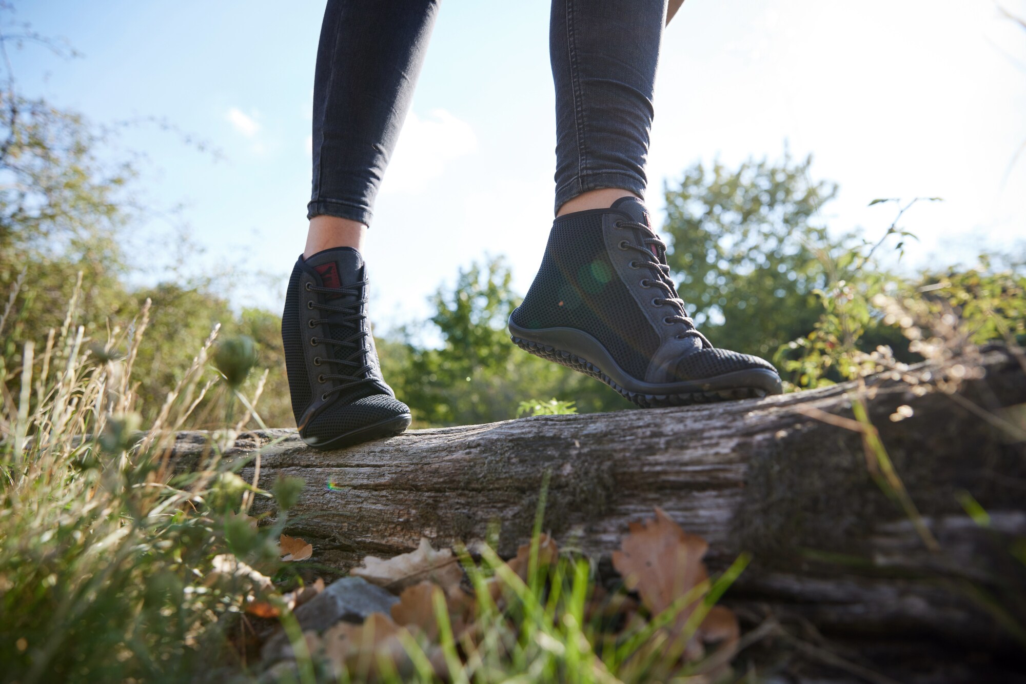 Eine balancierende Person in Barfußschuhen auf einem liegenden Baumstamm