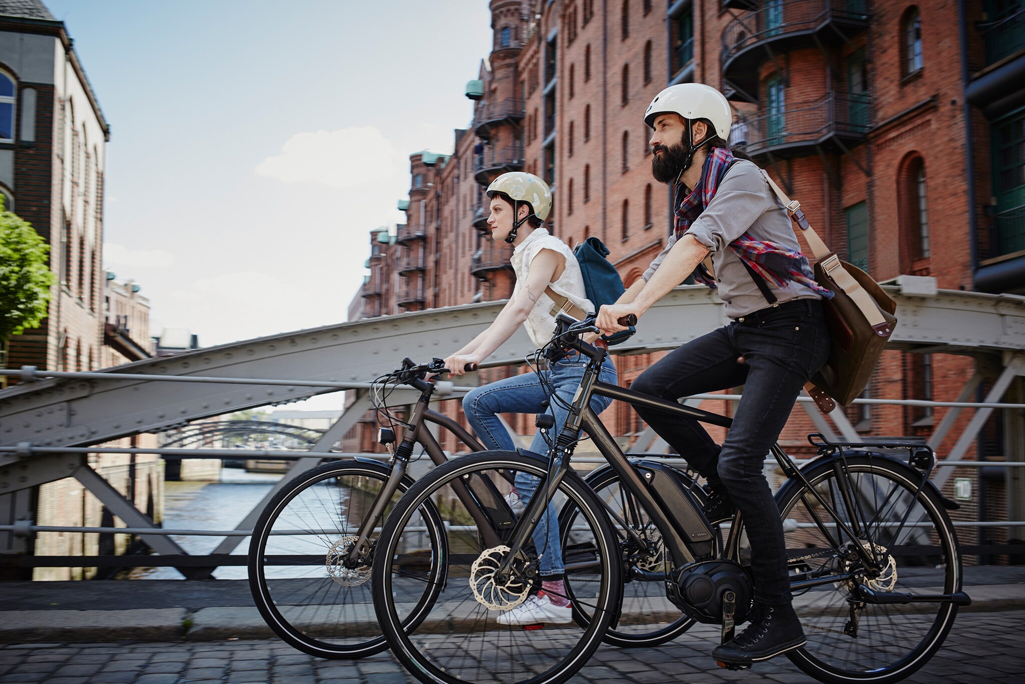 Ein Mann und eine Frau mit Fahrradhelmen fahren auf E-Bikes durch die Hamburger Speicherstadt. Ein Mann und eine Frau mit Fahrradhelmen fahren auf E-Bikes durch die Hamburger Speicherstadt.