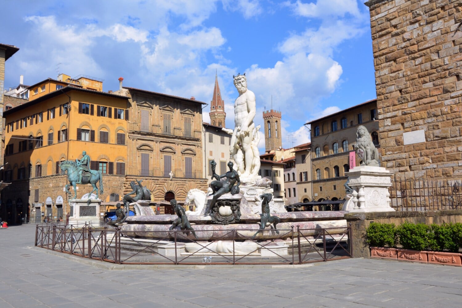 Ein Brunnen mit mythologischen Statuen am Rande eines Platzes Ein Brunnen mit mythologischen Statuen am Rande eines Platzes