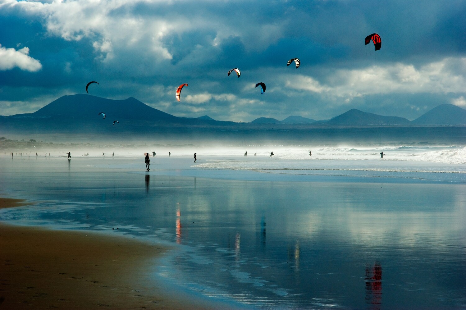 Ein bewölkter Sandstrand mit Kitesurfenden im Wasser Ein bewölkter Sandstrand mit Kitesurfenden im Wasser