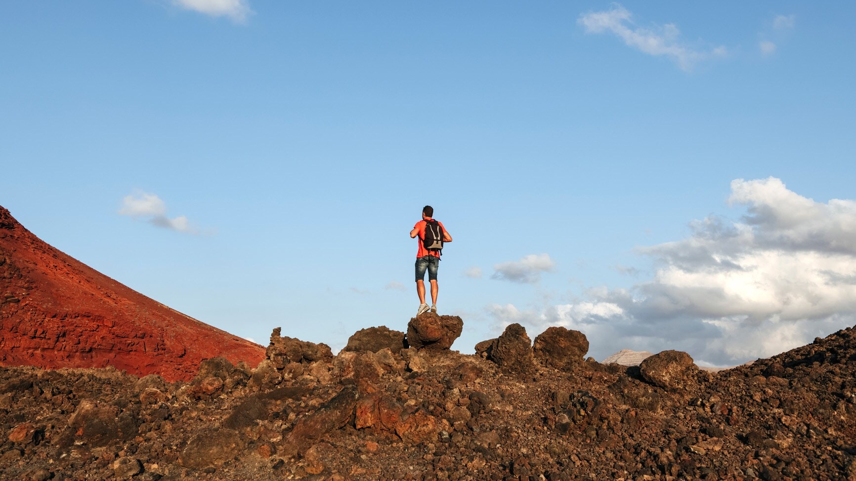 Rückansicht eines Mannes mit Rucksack auf einem rötlichen Felsen Rückansicht eines Mannes mit Rucksack auf einem rötlichen Felsen