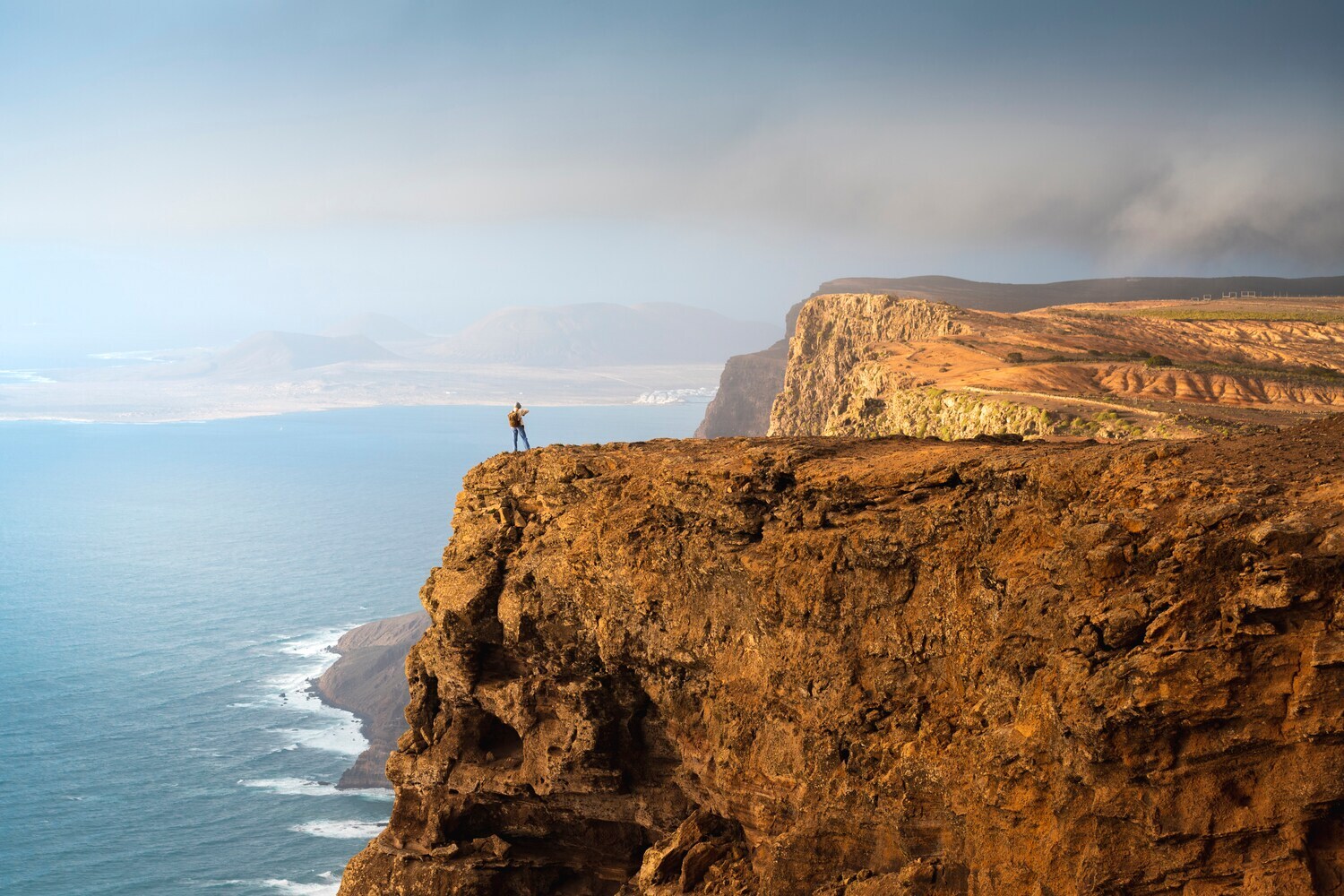 Küstenpanorama mit steiler Felsklippe, auf der eine Person steht