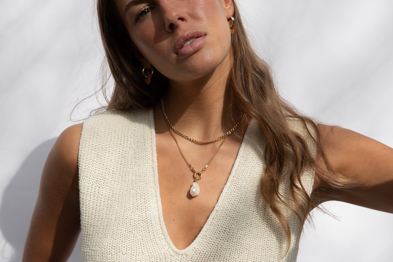 Eine Frau im hellen Strickoberteil trägt Perlenkette und Kreolen Eine Frau im hellen Strickoberteil trägt Perlenkette und Kreolen