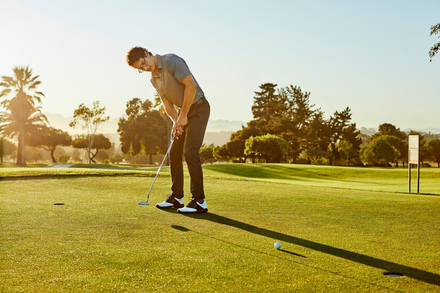 Ein Mann steht auf einem Golfplatzt und locht gerade den Golfball ein.