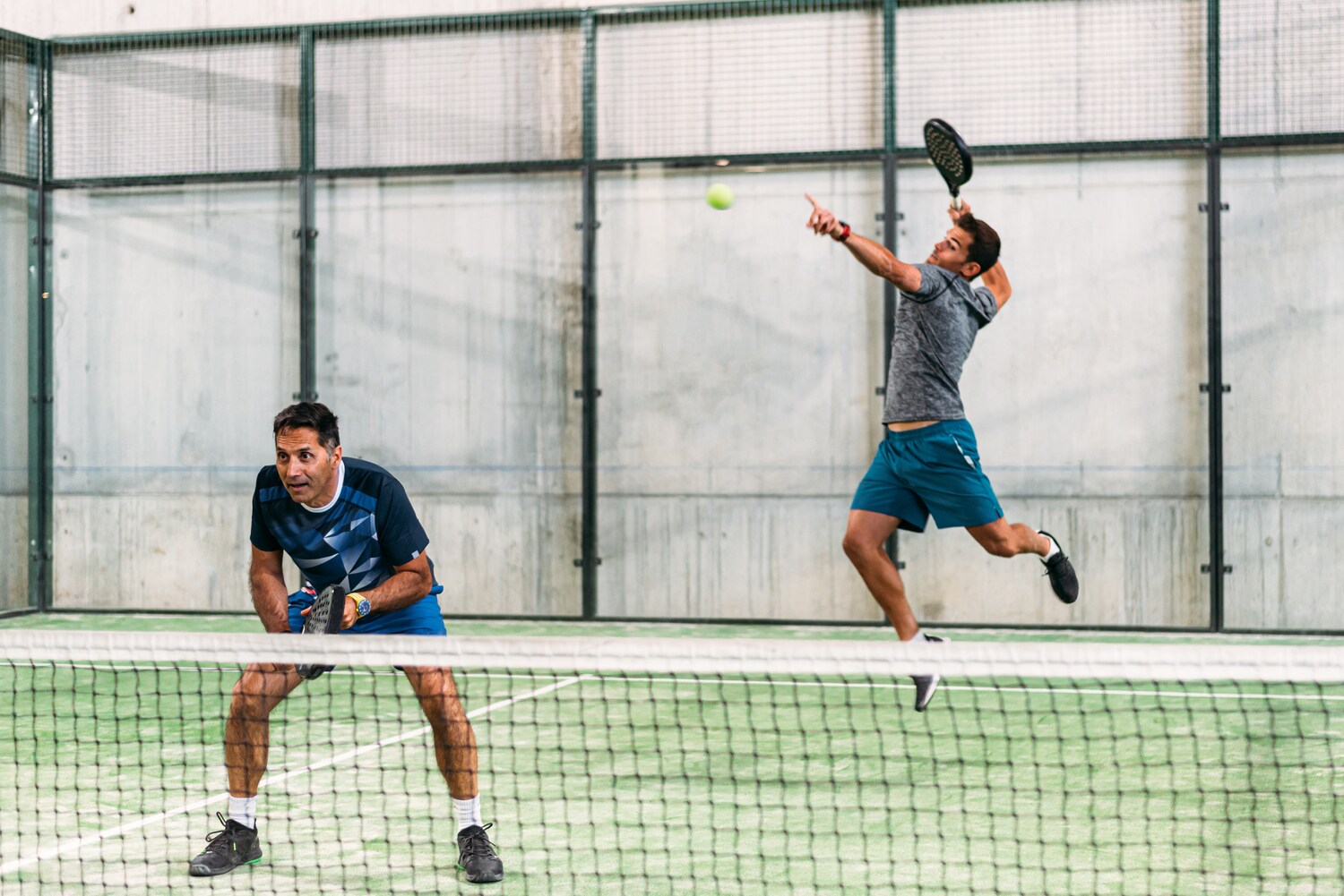 Zwei Männer spielen Padel-Tennis, von denen einer gerade einen Aufschlag macht. Zwei Männer spielen Padel-Tennis, von denen einer gerade einen Aufschlag macht.