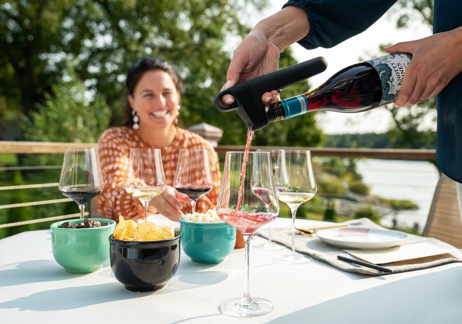 Eine Person gießt Rotwein aus einer Weinflasche mit einem Aufsatz in ein Glas auf einem gedeckten Tisch auf einer Terrasse