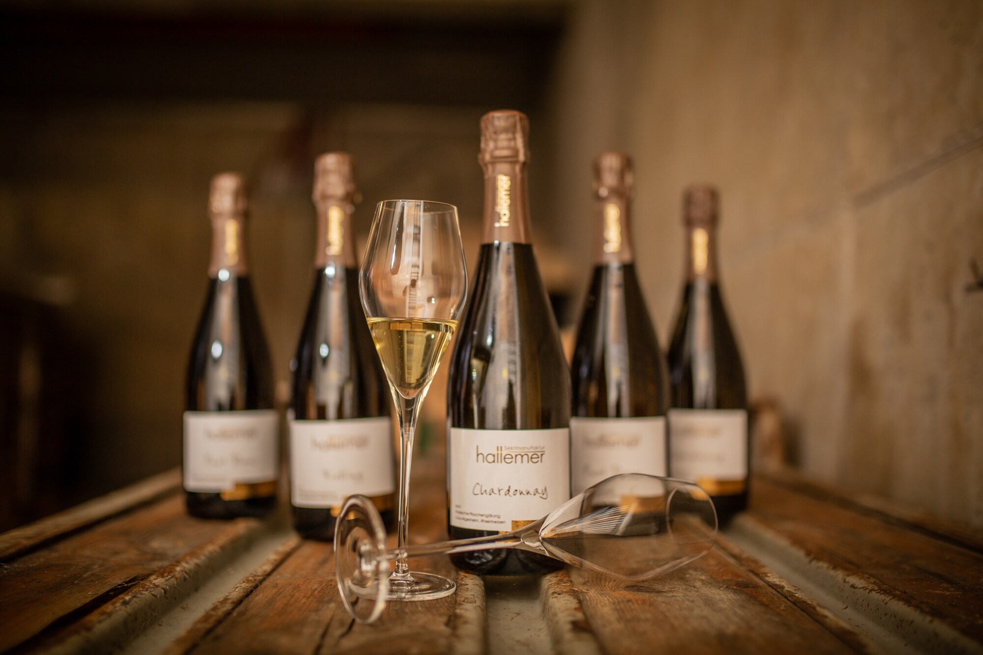 Fünf Winzersektflaschen mit zwei Gläsern in einem rustikalen Ambiente