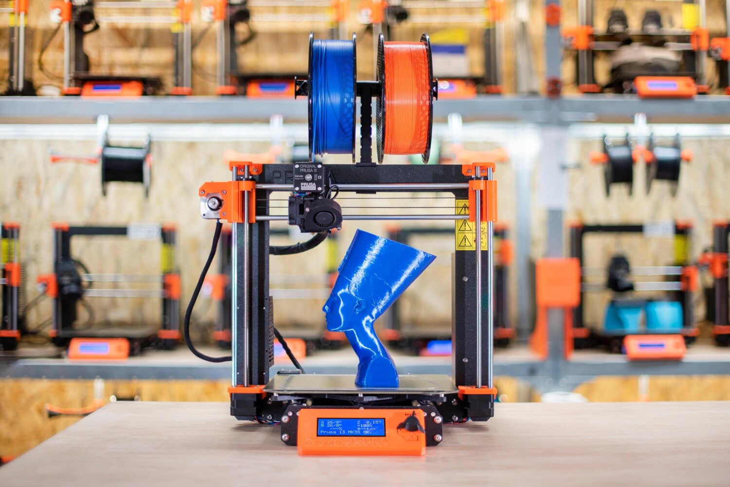 Ein 3D-Drucker mit Filament-Spulen und einer kleinen, gedruckten Nofretete-Büste aus blauem Kunststoff Ein 3D-Drucker mit Filament-Spulen und einer kleinen, gedruckten Nofretete-Büste aus blauem Kunststoff