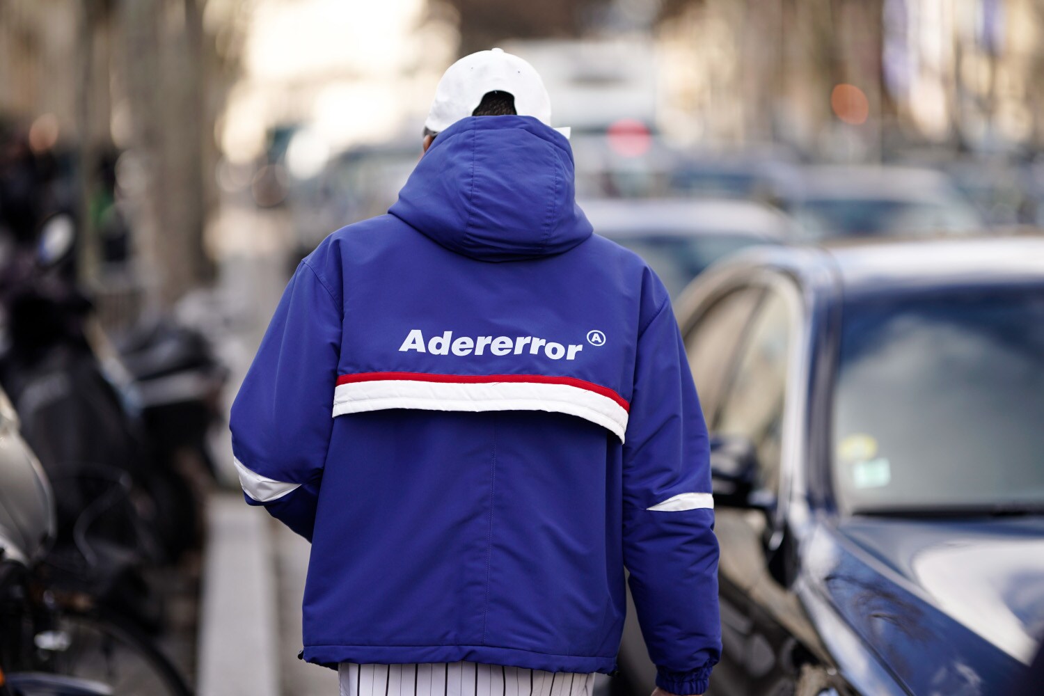 Rückansicht eines Mannes auf einer Straße mit blauer Trainingsjacke mit dem Markennamen Adererror