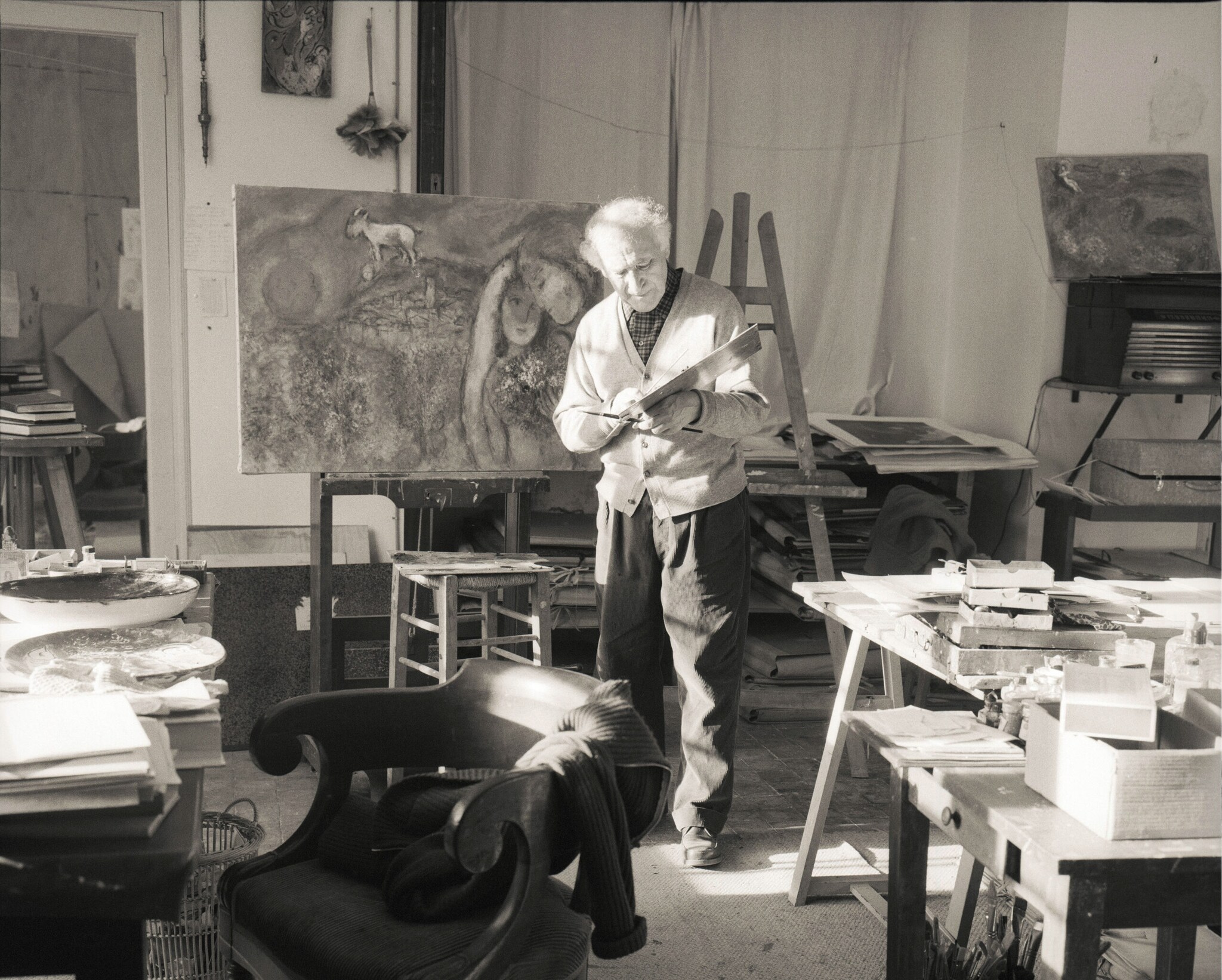 Historische Schwarzweiß-Fotografie des Malers Marc Chagall in seinem Studio vor einem Gemälde (1957) Historische Schwarzweiß-Fotografie des Malers Marc Chagall in seinem Studio vor einem Gemälde (1957)