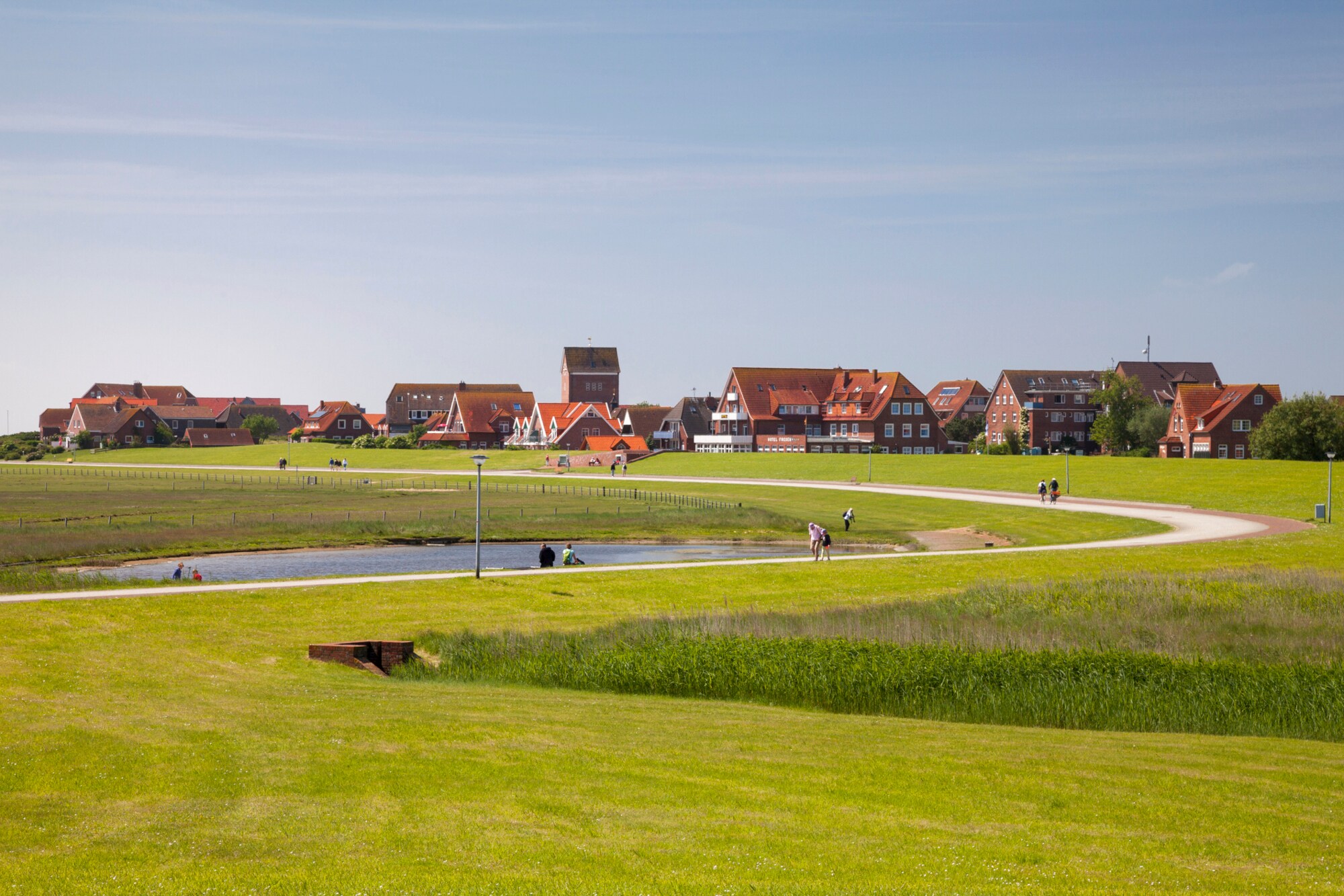 Eine flache Graslandschaft mit Spaziergängern und einem Ort im Hintergrund Eine flache Graslandschaft mit Spaziergängern und einem Ort im Hintergrund