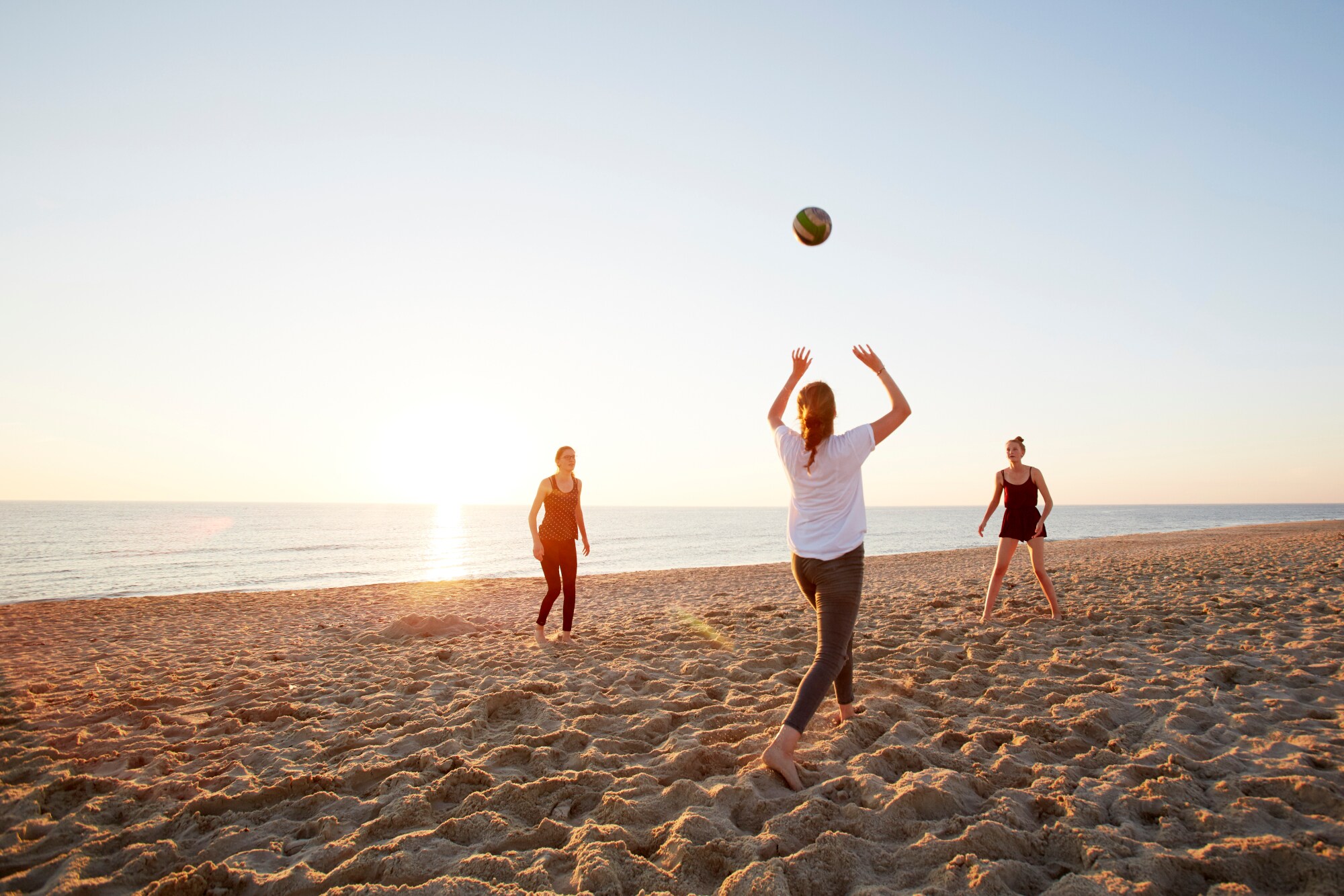Drei Jugendliche spielen Volleyball an einem weiten Sandstrand bei Sonnenuntergang