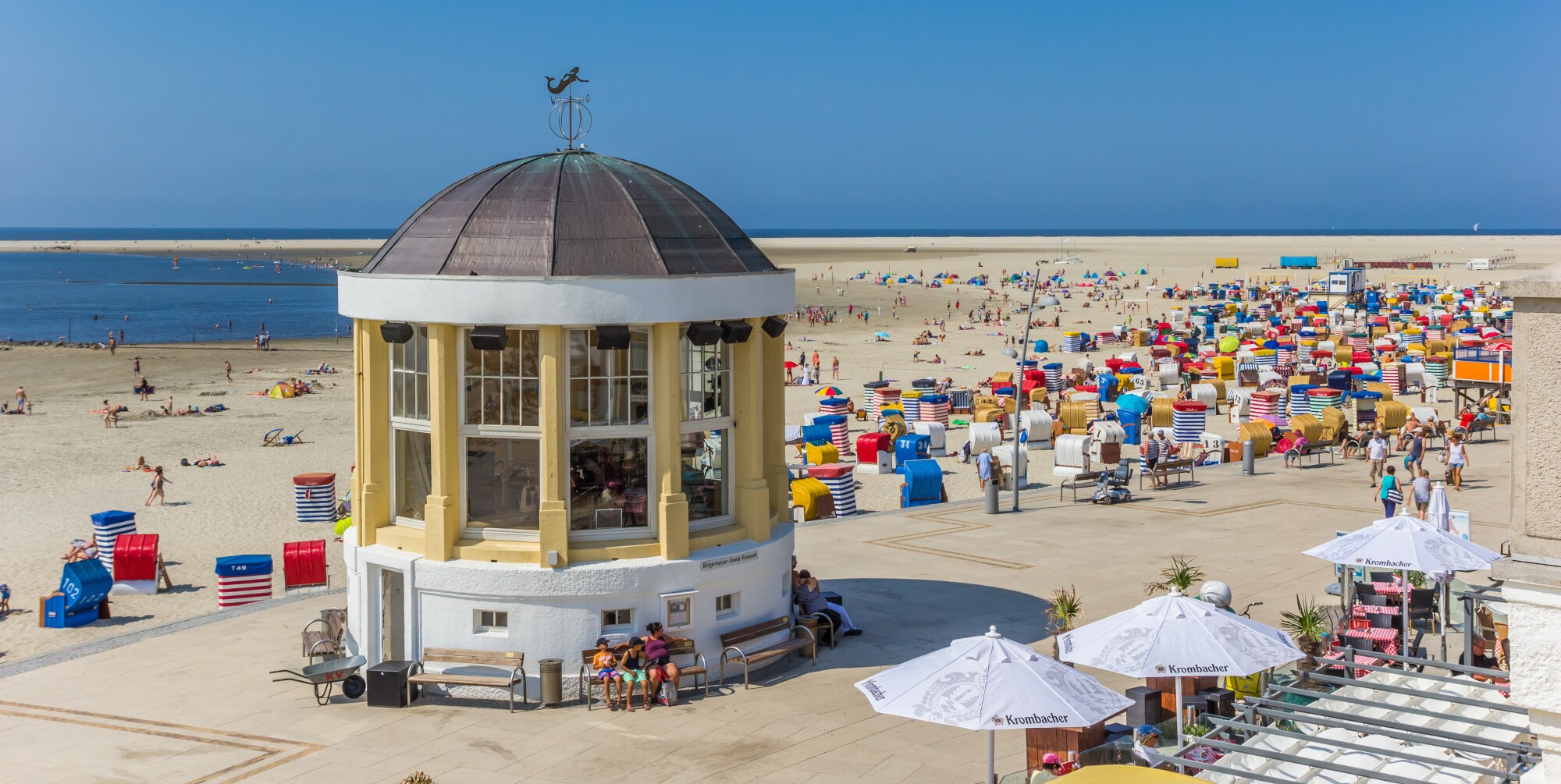 Eine Promenade mit Musikpavillon an einem Sandstrand mit bunten Strandkörben