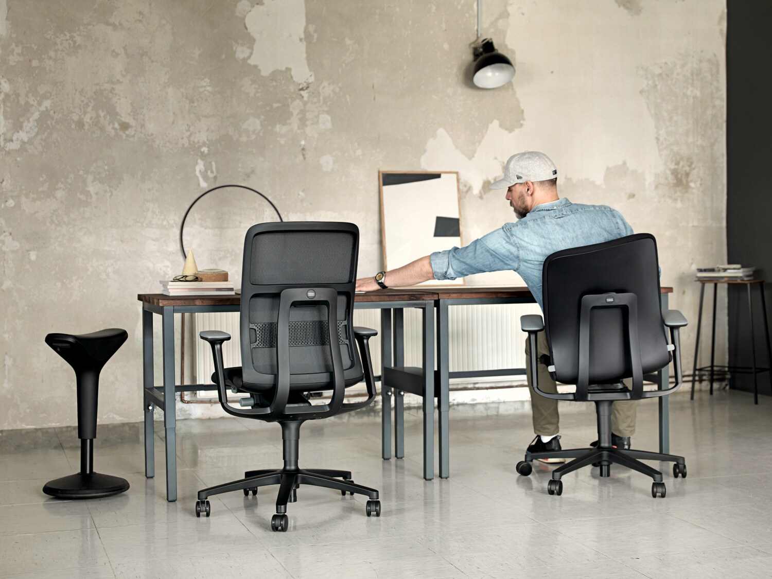 Rückansicht eines Mannes an einem Schreibtisch auf einem Schreibtischstuhl mit beweglicher Sitzfläche Rückansicht eines Mannes an einem Schreibtisch auf einem Schreibtischstuhl mit beweglicher Sitzfläche