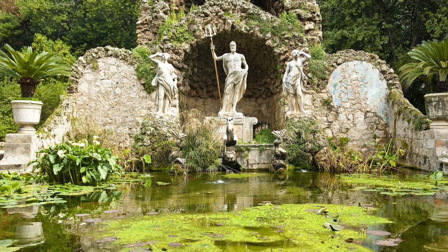 Ein Teich mit einer Neptun-Statue in einem botanischen Garten Ein Teich mit einer Neptun-Statue in einem botanischen Garten