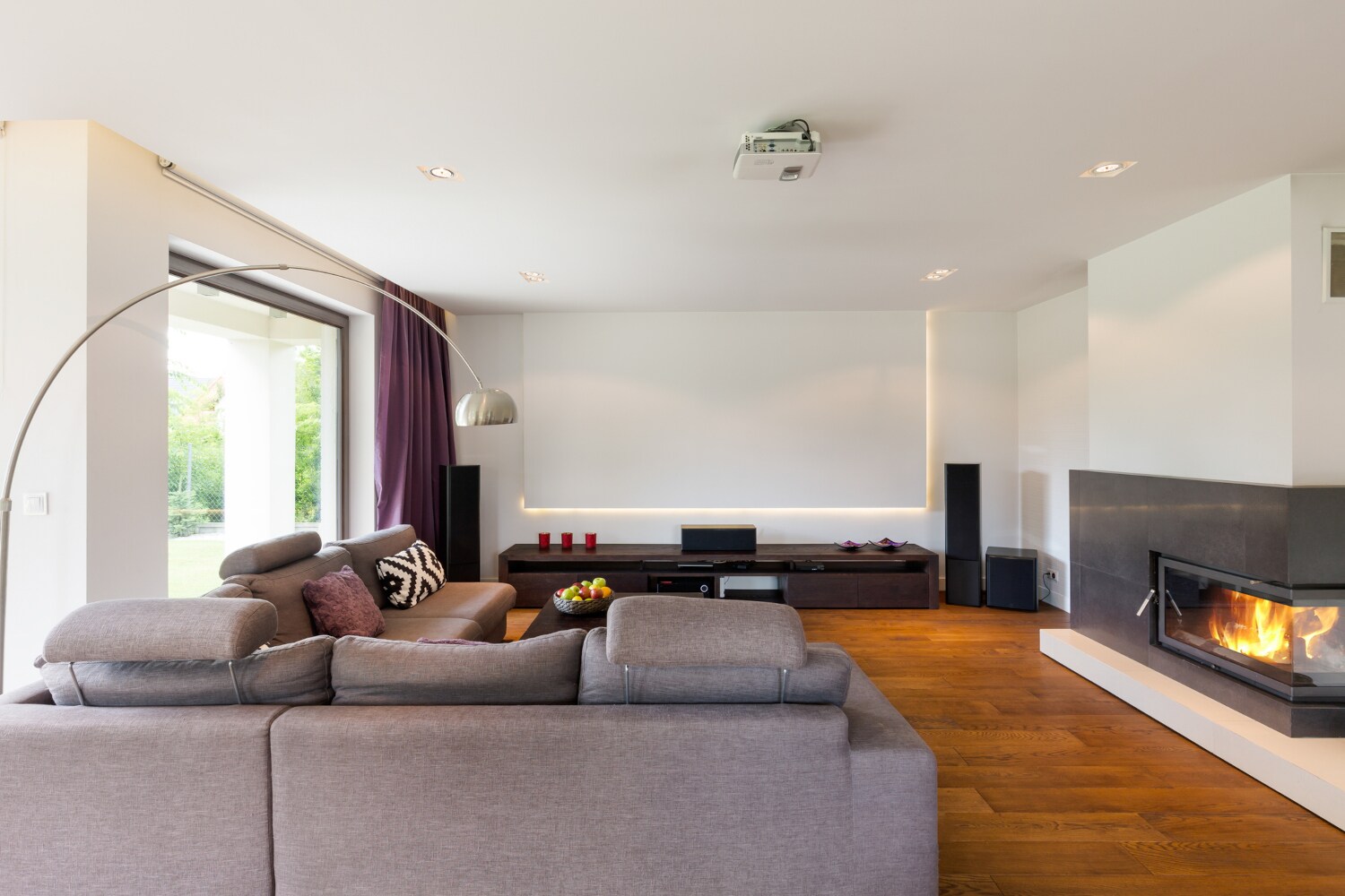 Ein modernes, großräumiges Wohnzimmer mit einer großen Leinwand und einem Beamer an der Decke