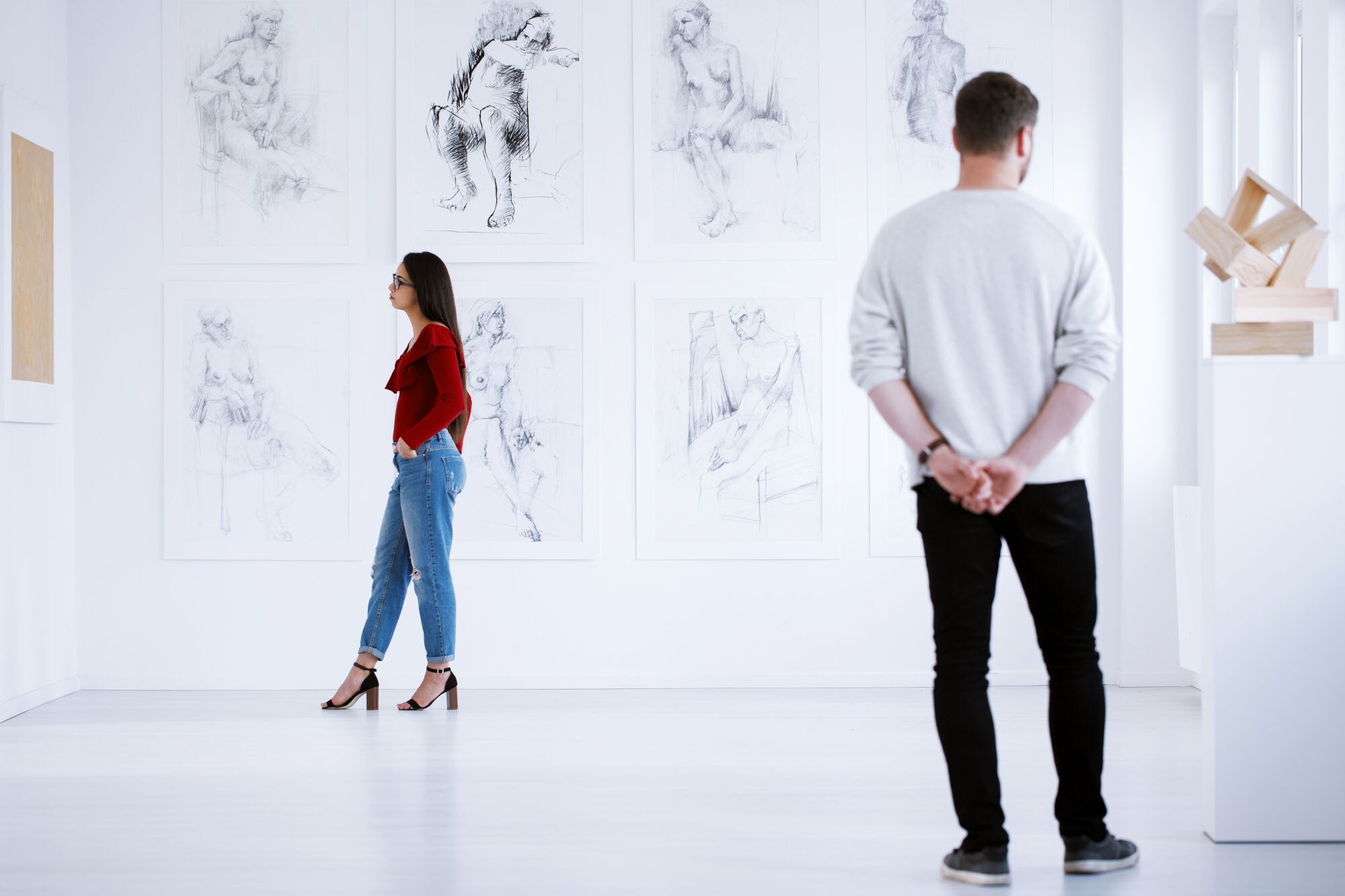 Zwei Personen schauen sich in einem weißen Ausstellungsraum Zeichnungen und Skulpturen an Zwei Personen schauen sich in einem weißen Ausstellungsraum Zeichnungen und Skulpturen an