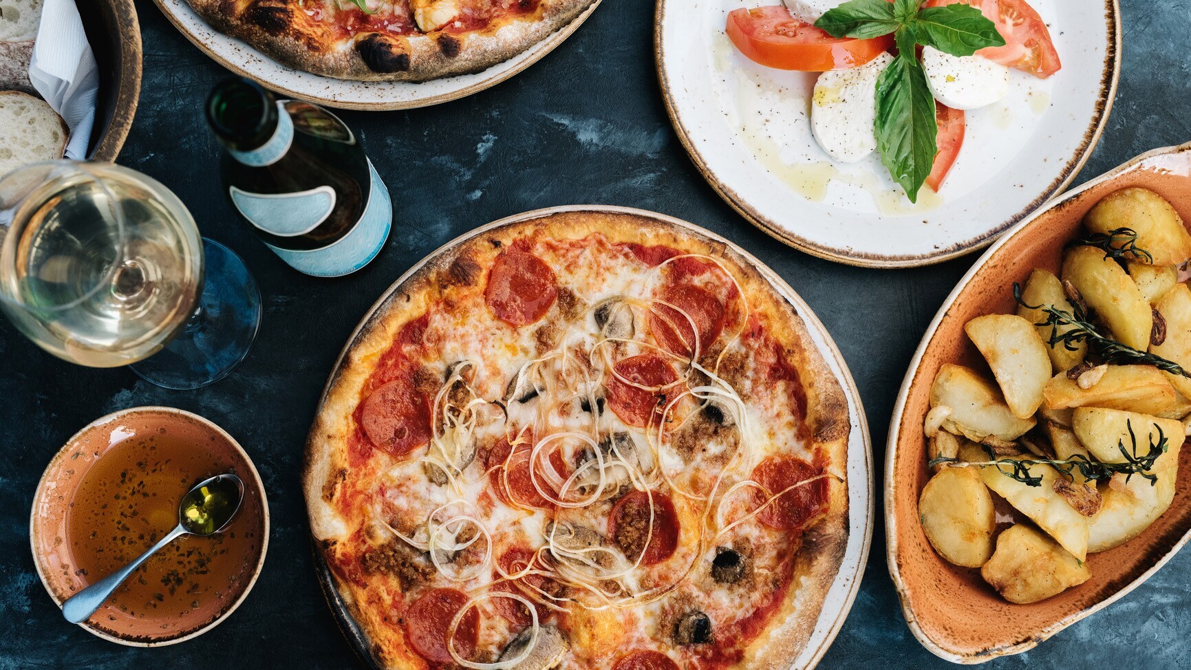 Aufsicht einer Pizza neben weiteren italienischen Gerichten und einem Glas Wein auf einem Tisch Aufsicht einer Pizza neben weiteren italienischen Gerichten und einem Glas Wein auf einem Tisch