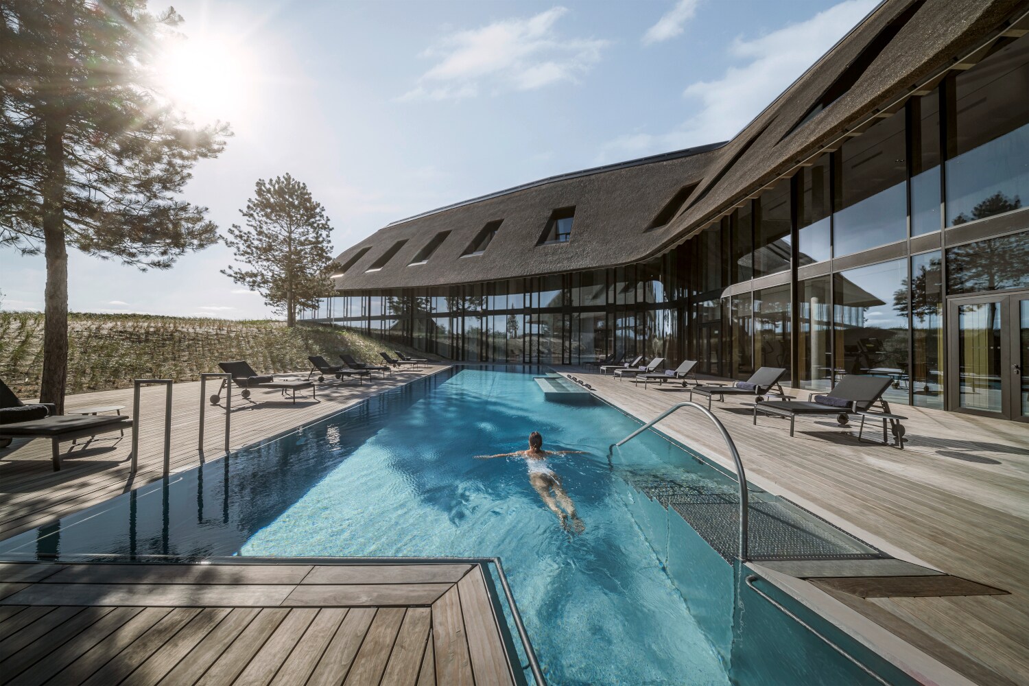 Ein luxuriöses Hotel in den Dünen mit Reetdach und Außenpool, in dem eine Frau schwimmt