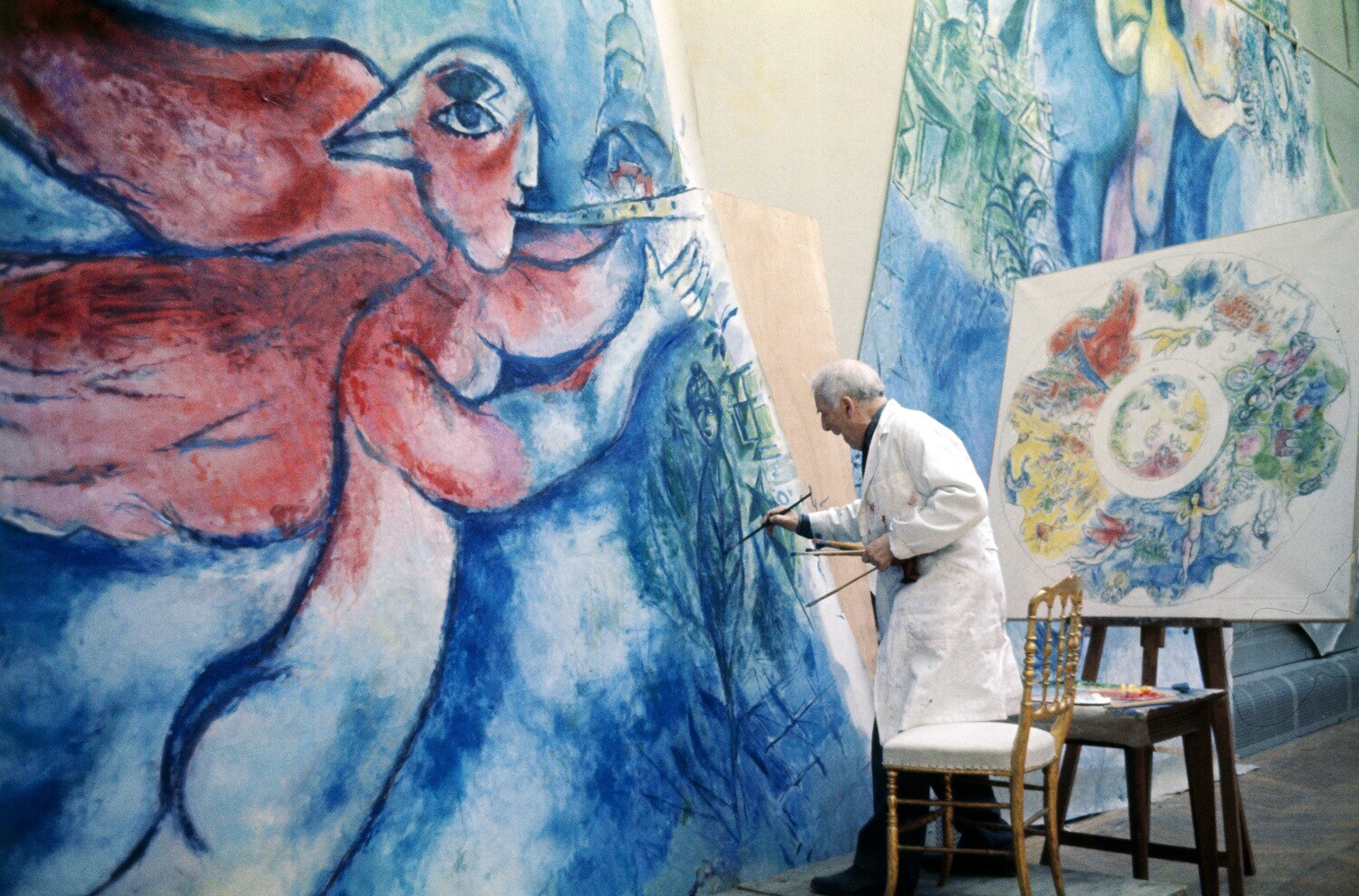 Marc Chagall malt in einem weißen Kittel an einer großen Leinwand, daneben eine Entwurfsskizze für ein Deckengemälde Marc Chagall malt in einem weißen Kittel an einer großen Leinwand, daneben eine Entwurfsskizze für ein Deckengemälde