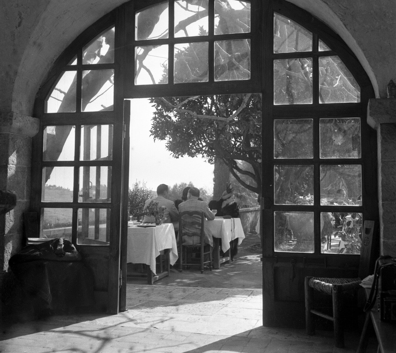 Historische Schwarzweiß-Fotografie des Restaurants La Colombe d’Or mit Gästen an einem Tisch auf der Terrasse (1949) Historische Schwarzweiß-Fotografie des Restaurants La Colombe d’Or mit Gästen an einem Tisch auf der Terrasse (1949)