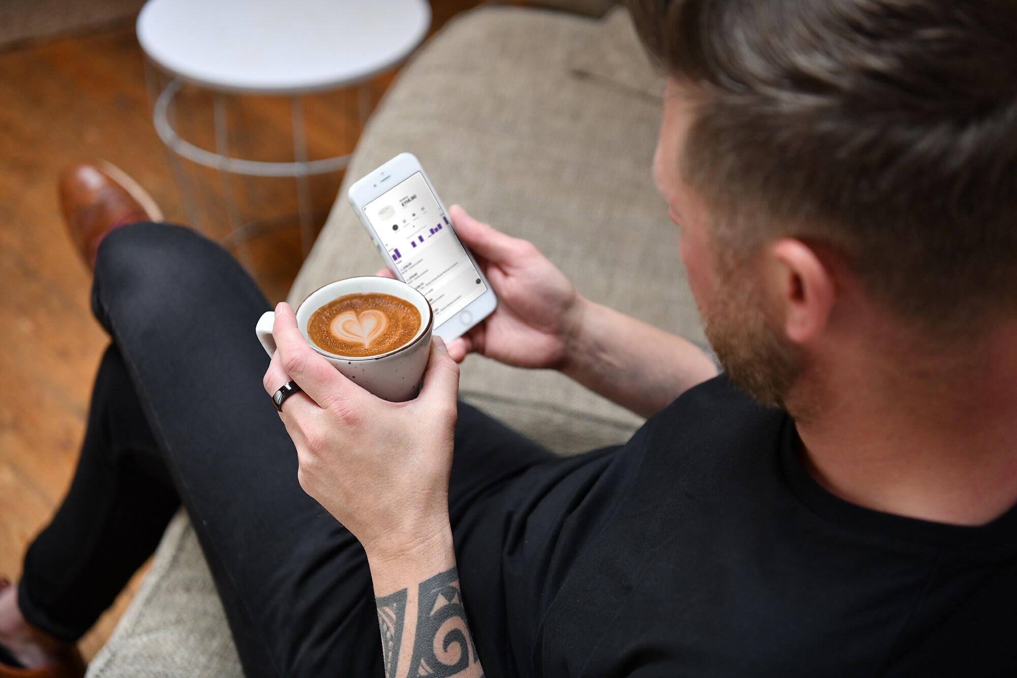 Ein Mann mit dunklem NFC-Ring hält einen Kaffee und ein Smartphone in der Hand.