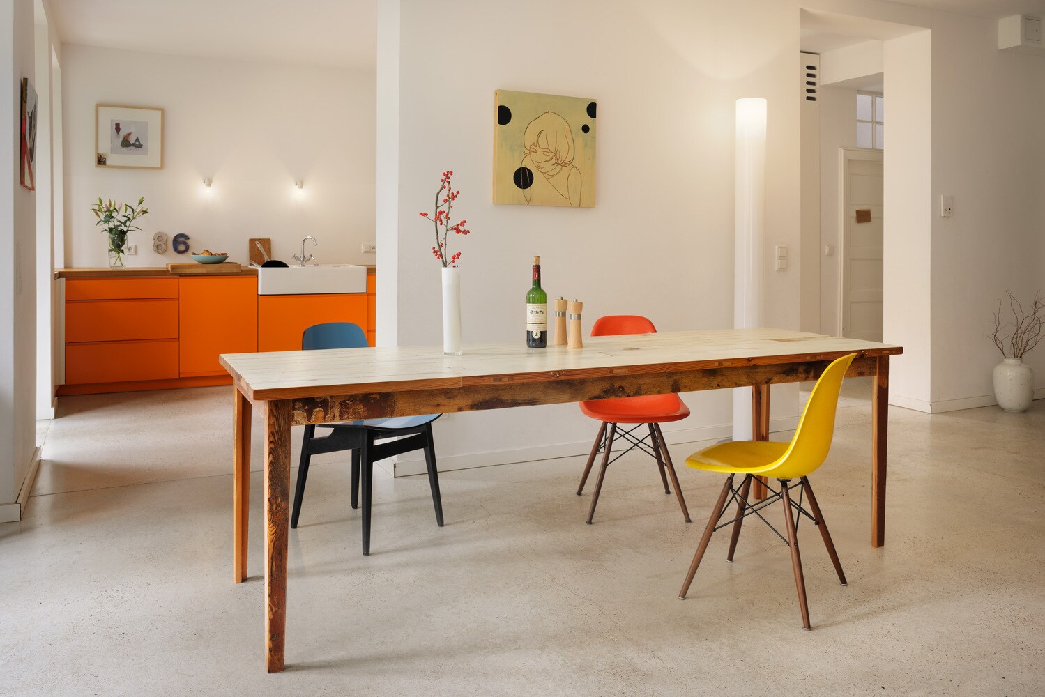 Blick in eine minimalistisch eingerichtete Wohnung mit Holztisch und drei bunten Stühlen.