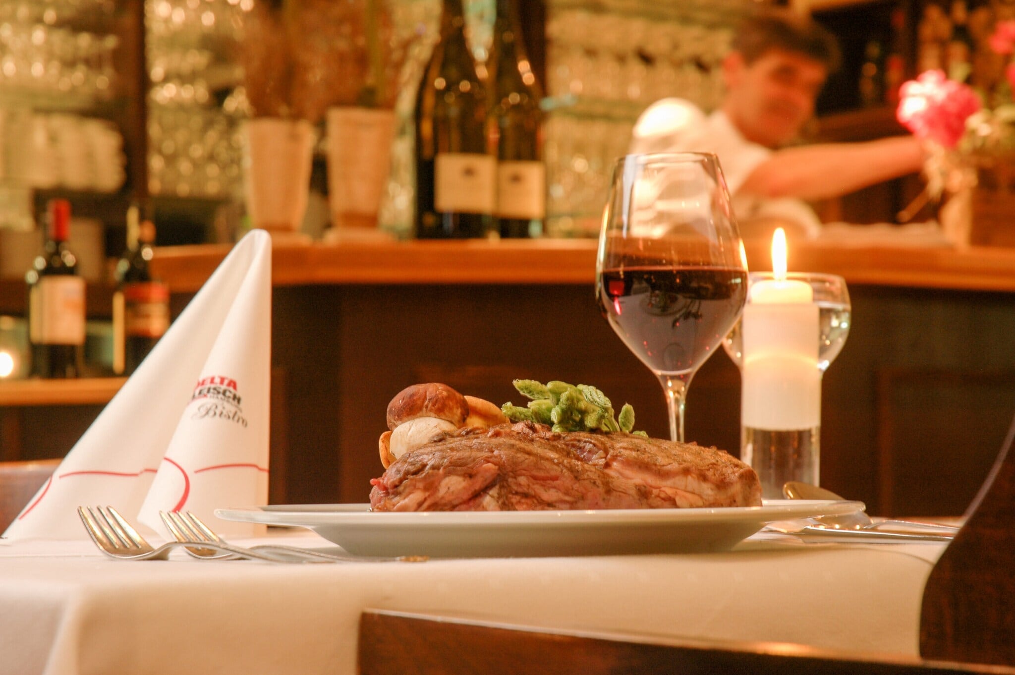 Ein gedeckter Restauranttisch mit Rotwein im Glas und Fleischgericht auf dem Teller. Ein gedeckter Restauranttisch mit Rotwein im Glas und Fleischgericht auf dem Teller.