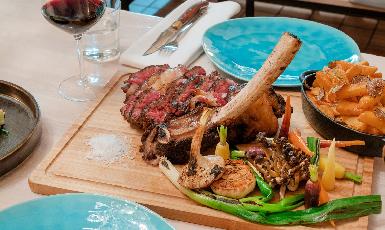 Ein auf einem Brett angerichtetes Steak mit gegrilltem Gemüse auf einem gedeckten Tisch Ein auf einem Brett angerichtetes Steak mit gegrilltem Gemüse auf einem gedeckten Tisch