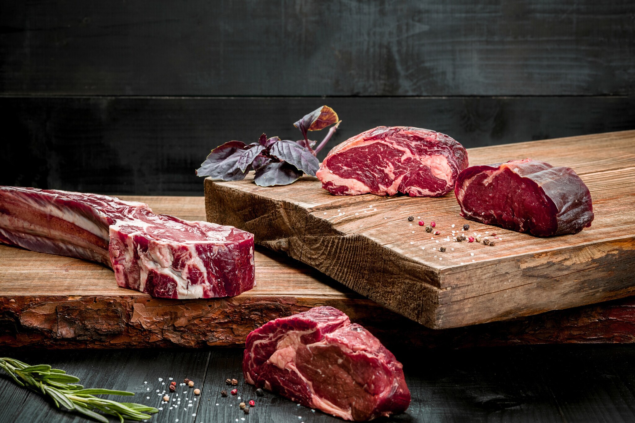 Rohes Rindfleisch auf Schneidebrett mit Gewürzen, frischem Basilikum und einem Zweig Rosmarin auf Holzgrund