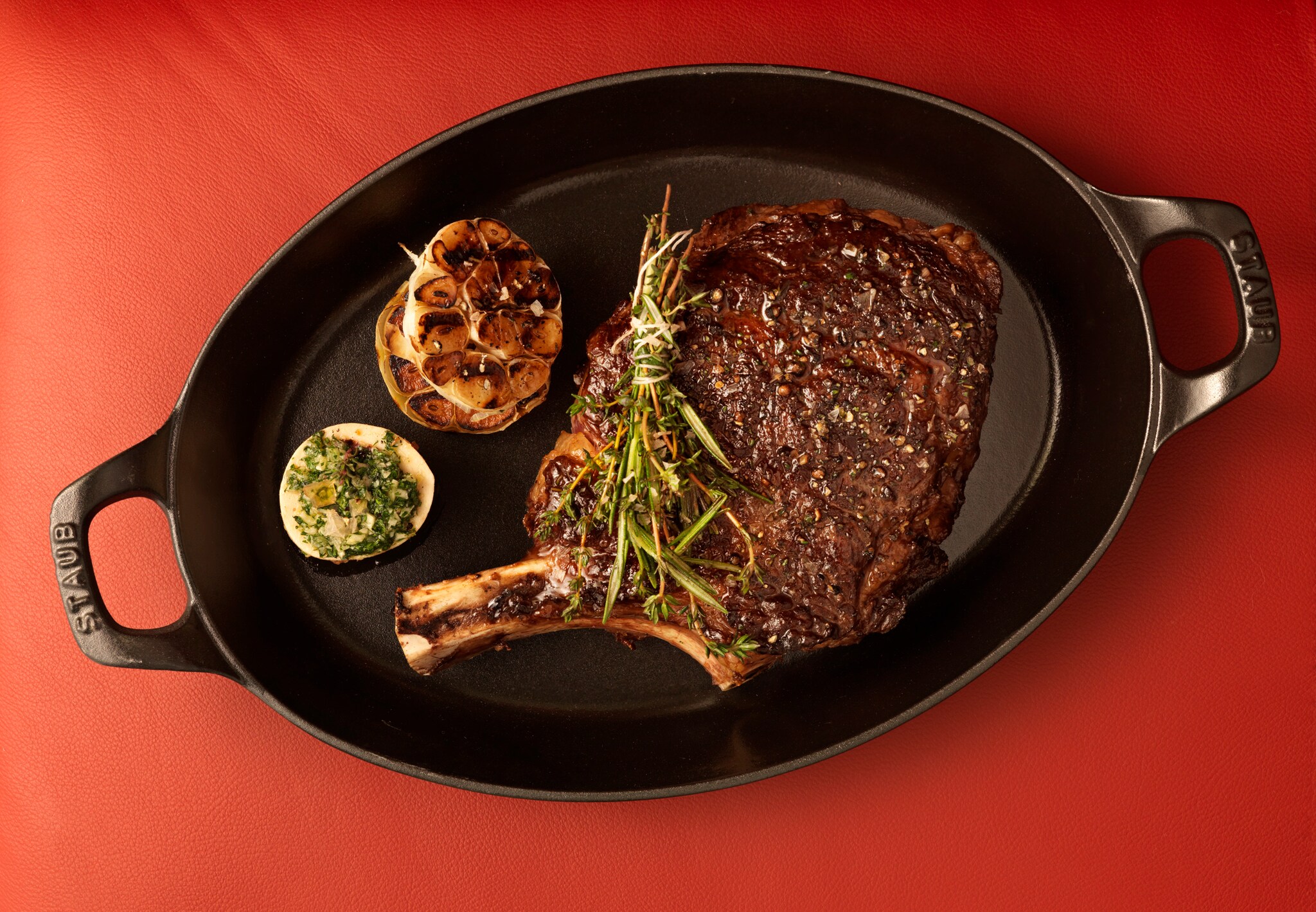 Ein zubereitetes Stück Fleisch in einem gusseisernen Behältnis, garniert mit Kräuter und Beilagen.