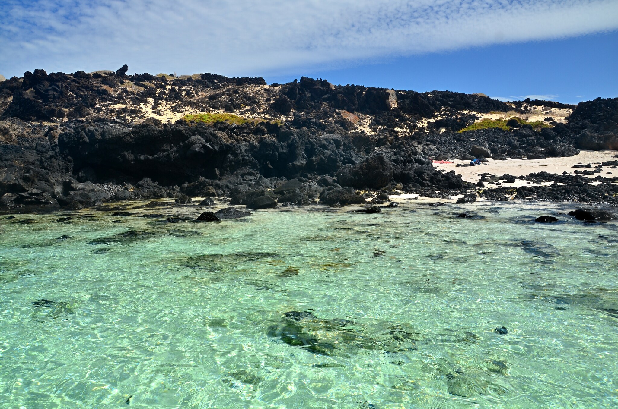 Blick auf den Strand von Caleton Blanco mit schwarzen Felsen und klarem Wasser