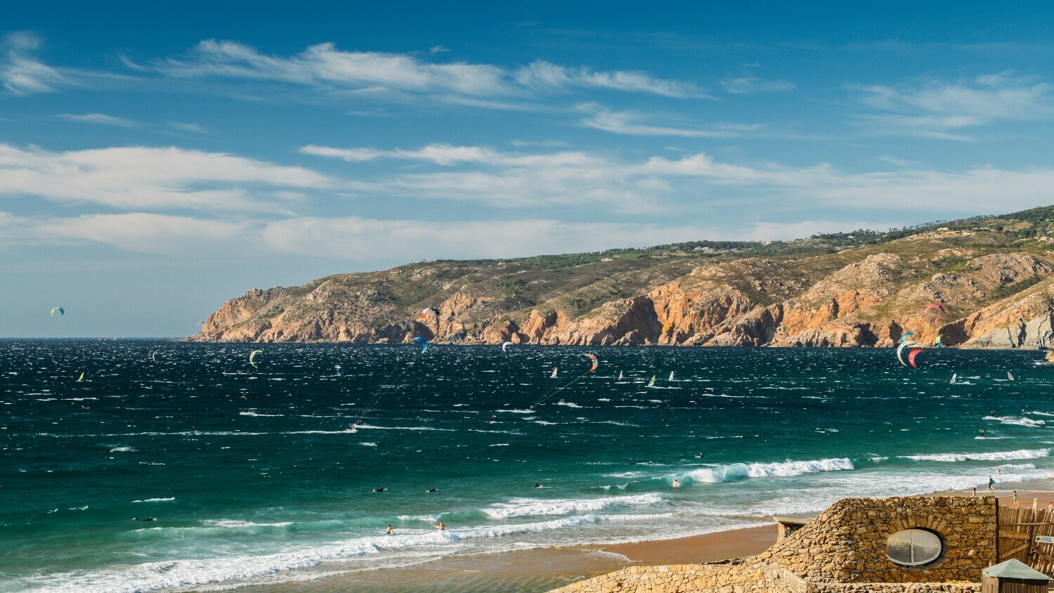 Eine felsige Meeresbucht mit Kitesurfenden im Wasser