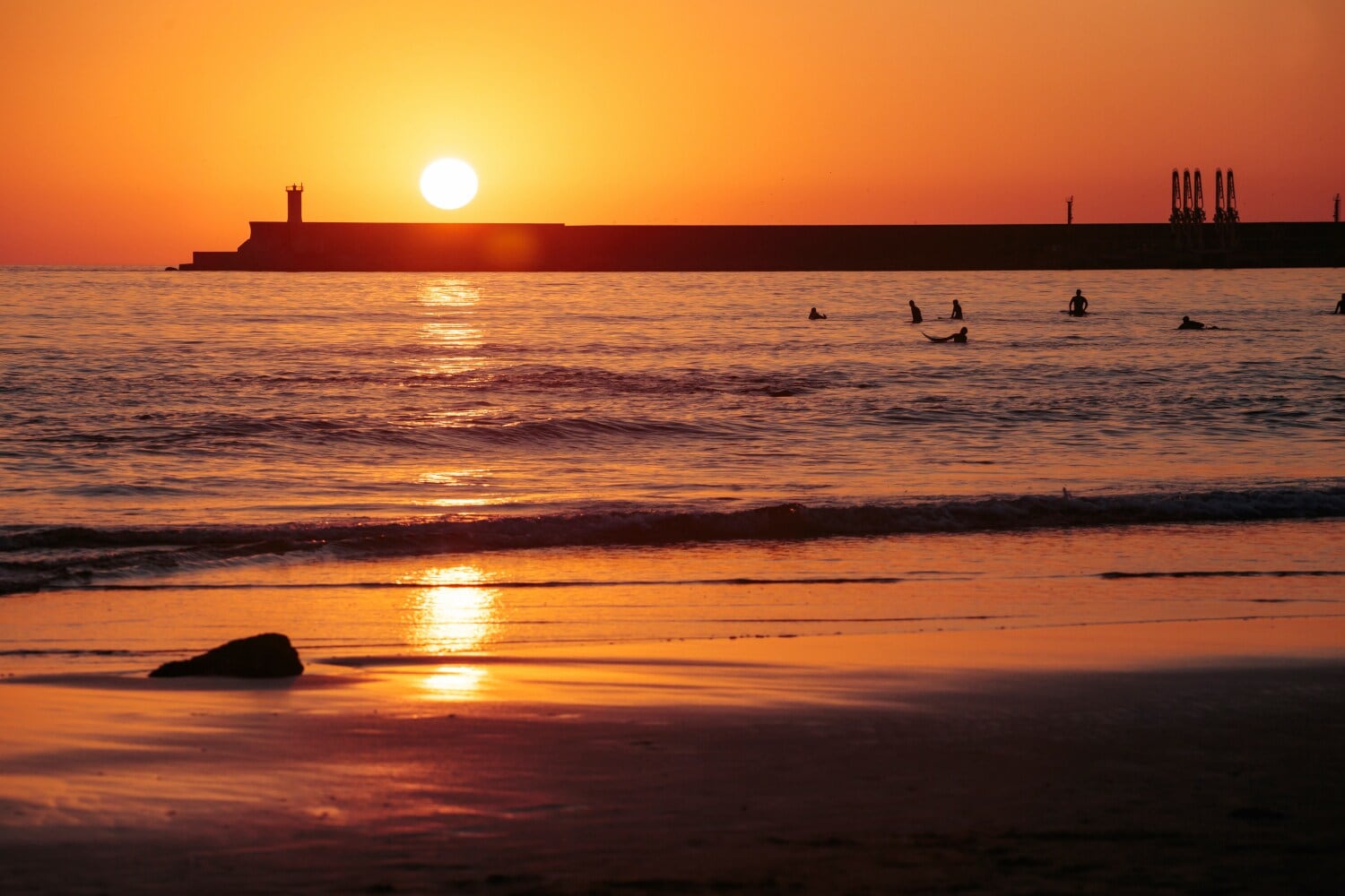 Personen treiben auf Surfbrettern am Strand im Wasser bei Sonnenuntergang Personen treiben auf Surfbrettern am Strand im Wasser bei Sonnenuntergang