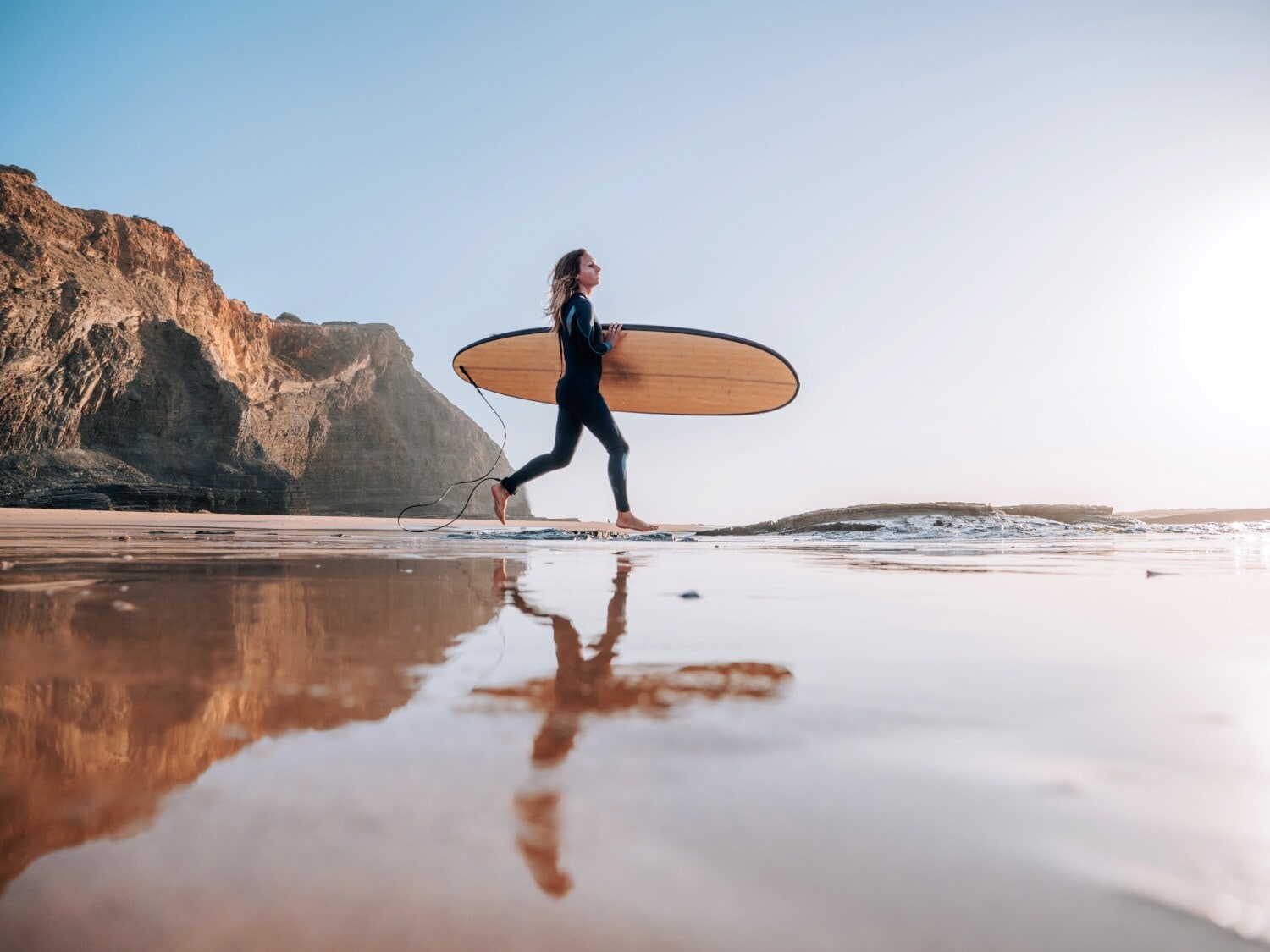 Eine Frau im Neoprenanzug trägt ihr Surfbrett unterm Arm ins Meer Eine Frau im Neoprenanzug trägt ihr Surfbrett unterm Arm ins Meer