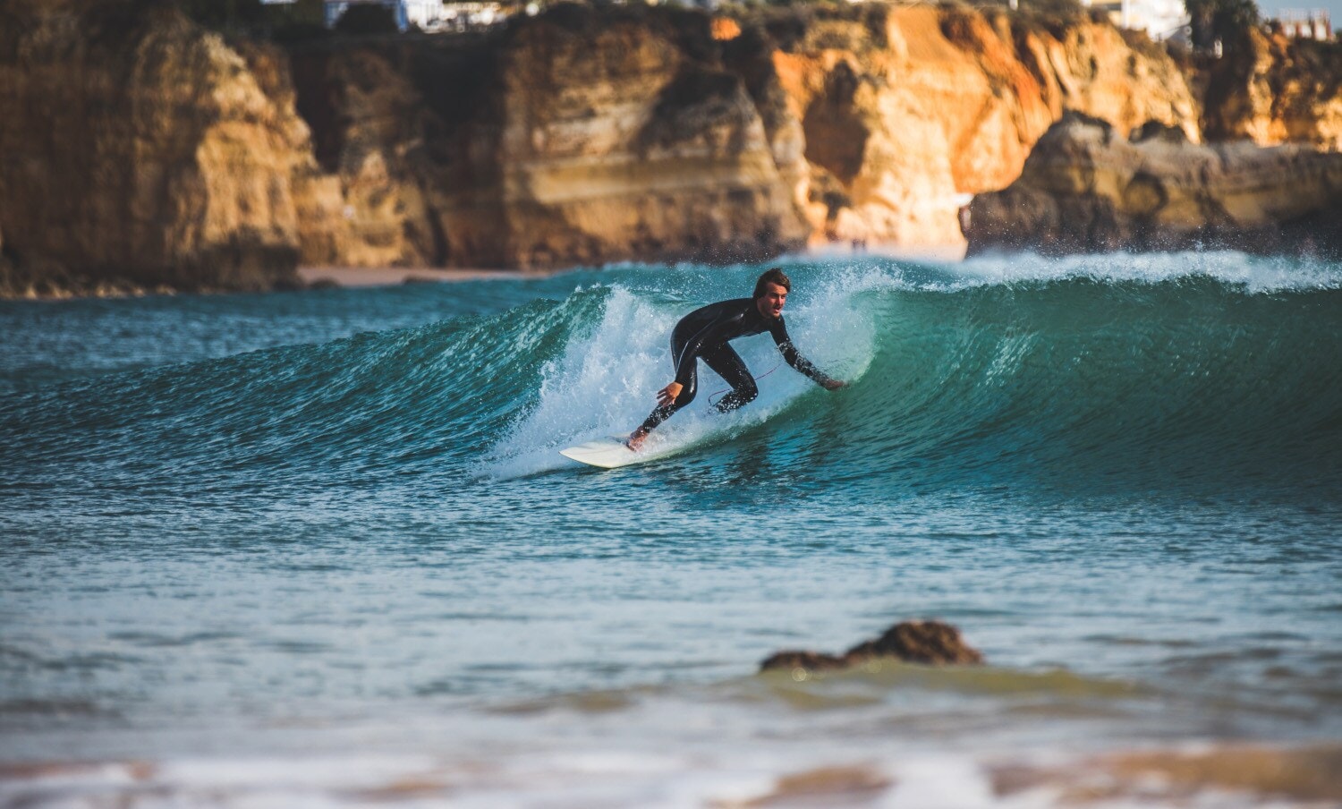 Ein Surfer im Neoprenanzug surft auf einer Welle im Meer vor einer Felsenküste Ein Surfer im Neoprenanzug surft auf einer Welle im Meer vor einer Felsenküste