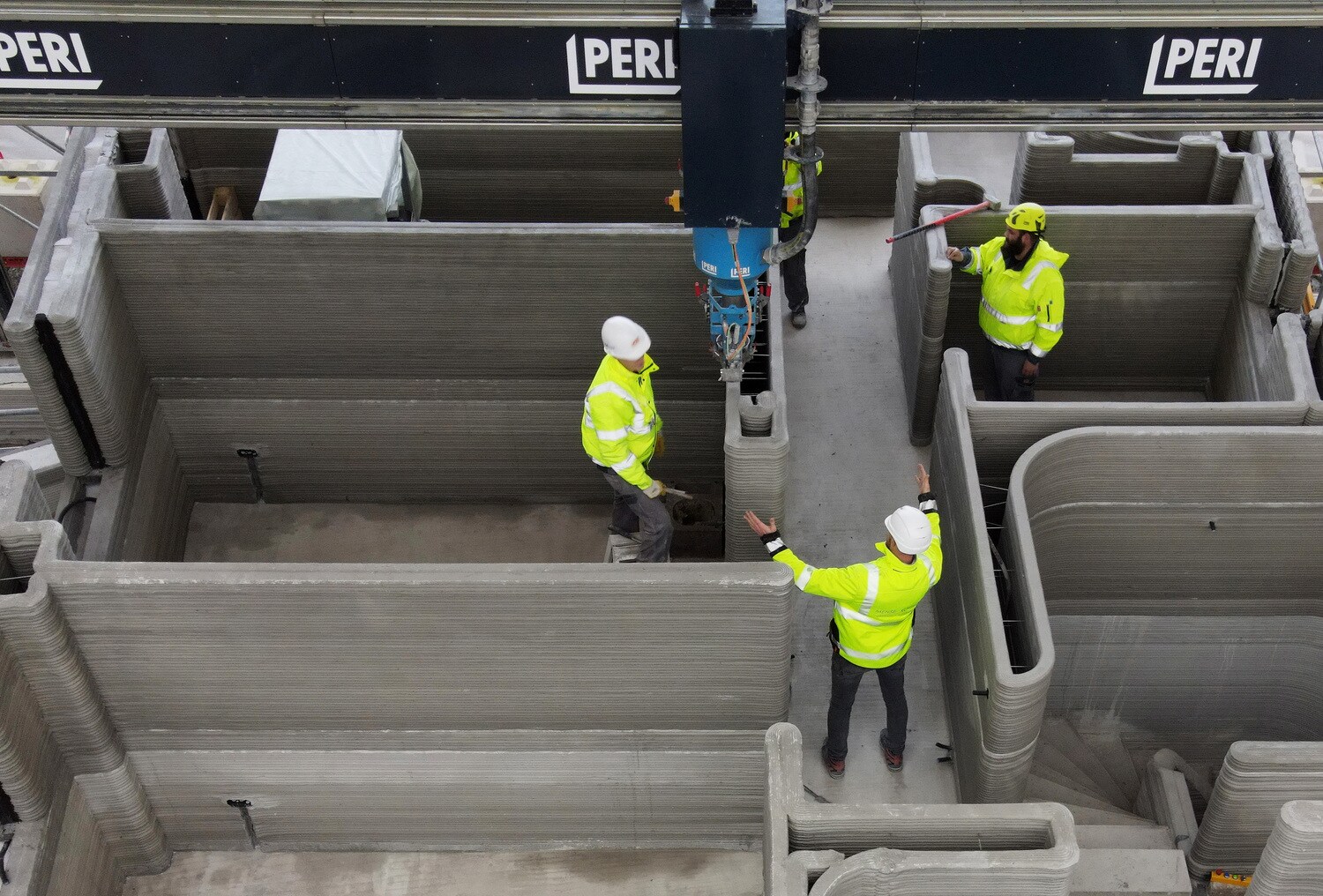Baustelle mit Bauarbeitern inmitten den Mauern eines Hauses, das mit einem 3D-Drucker erstellt wird