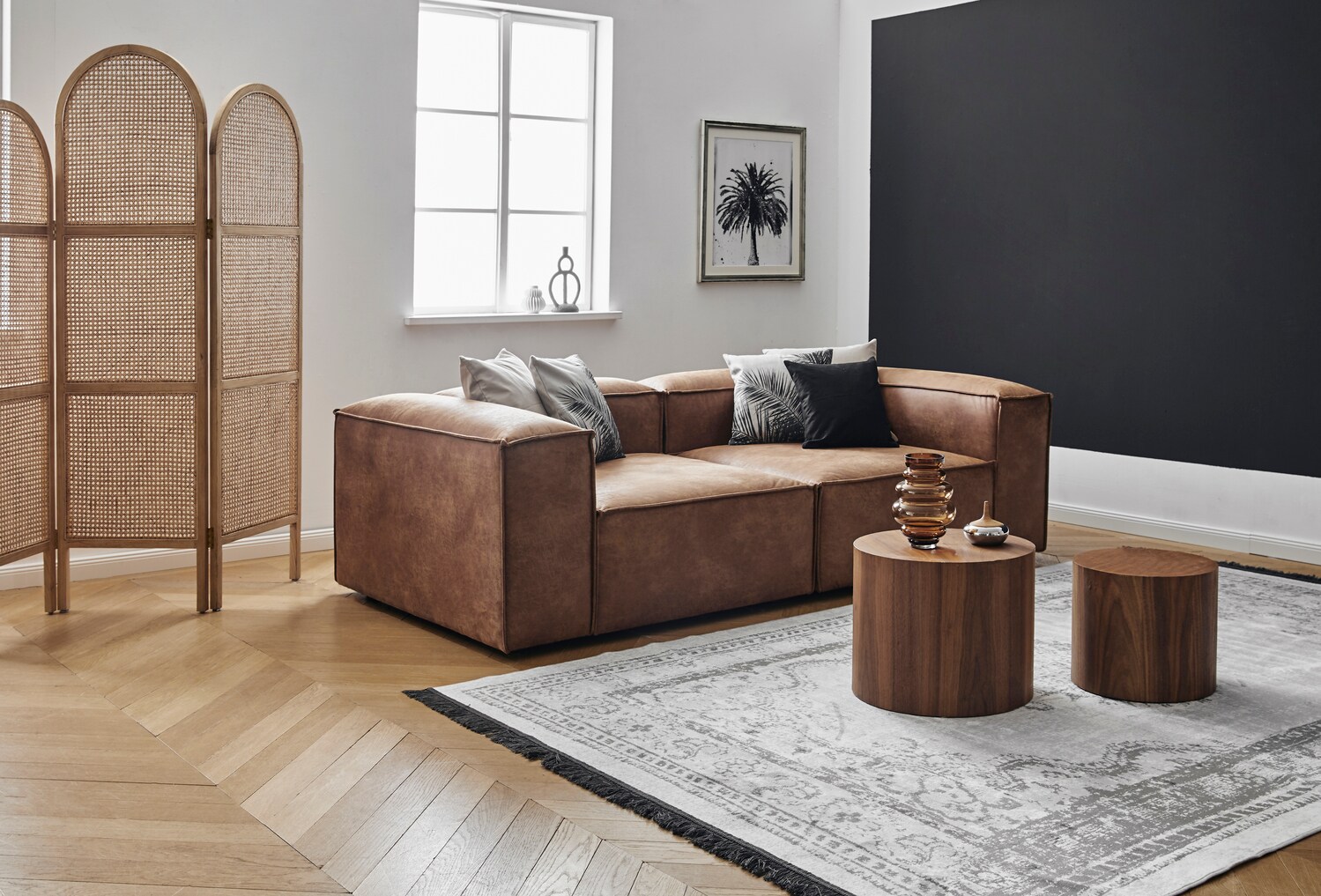 Ein helles, modernes Wohnzimmer mit einer braunen, kubischen Ledercouch und Beistelltischen aus dunklem Naturholz Ein helles, modernes Wohnzimmer mit einer braunen, kubischen Ledercouch und Beistelltischen aus dunklem Naturholz