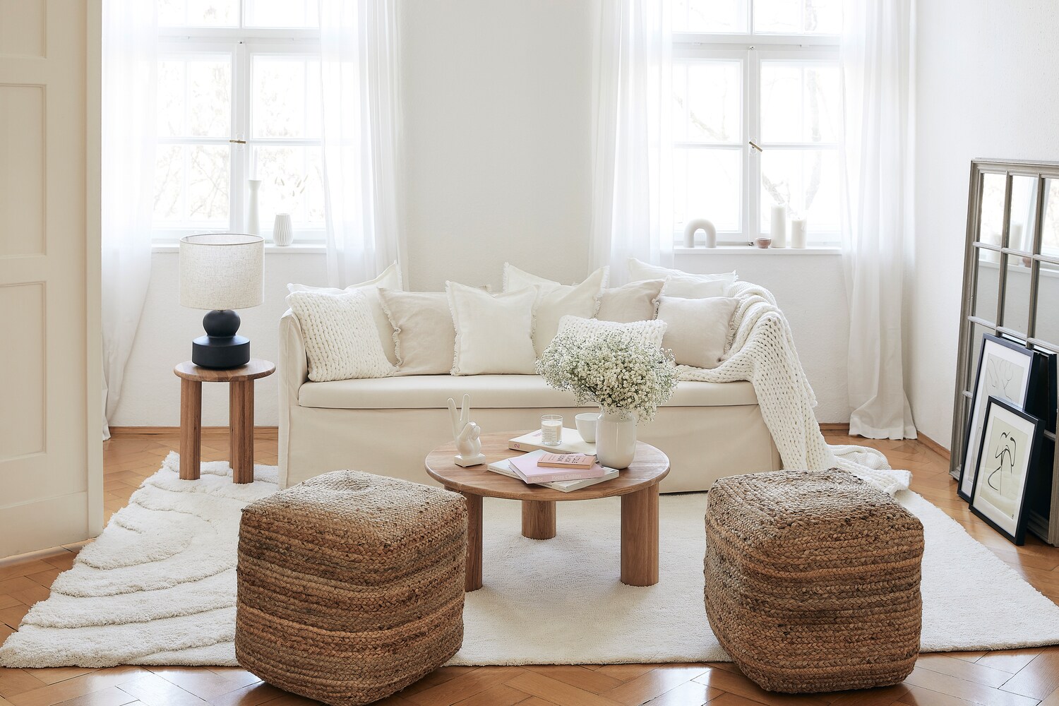 Ein lichtdurchflutetes Wohnzimmer mit einem weißen Stoffsofa und hellen Wohntextilien Ein lichtdurchflutetes Wohnzimmer mit einem weißen Stoffsofa und hellen Wohntextilien