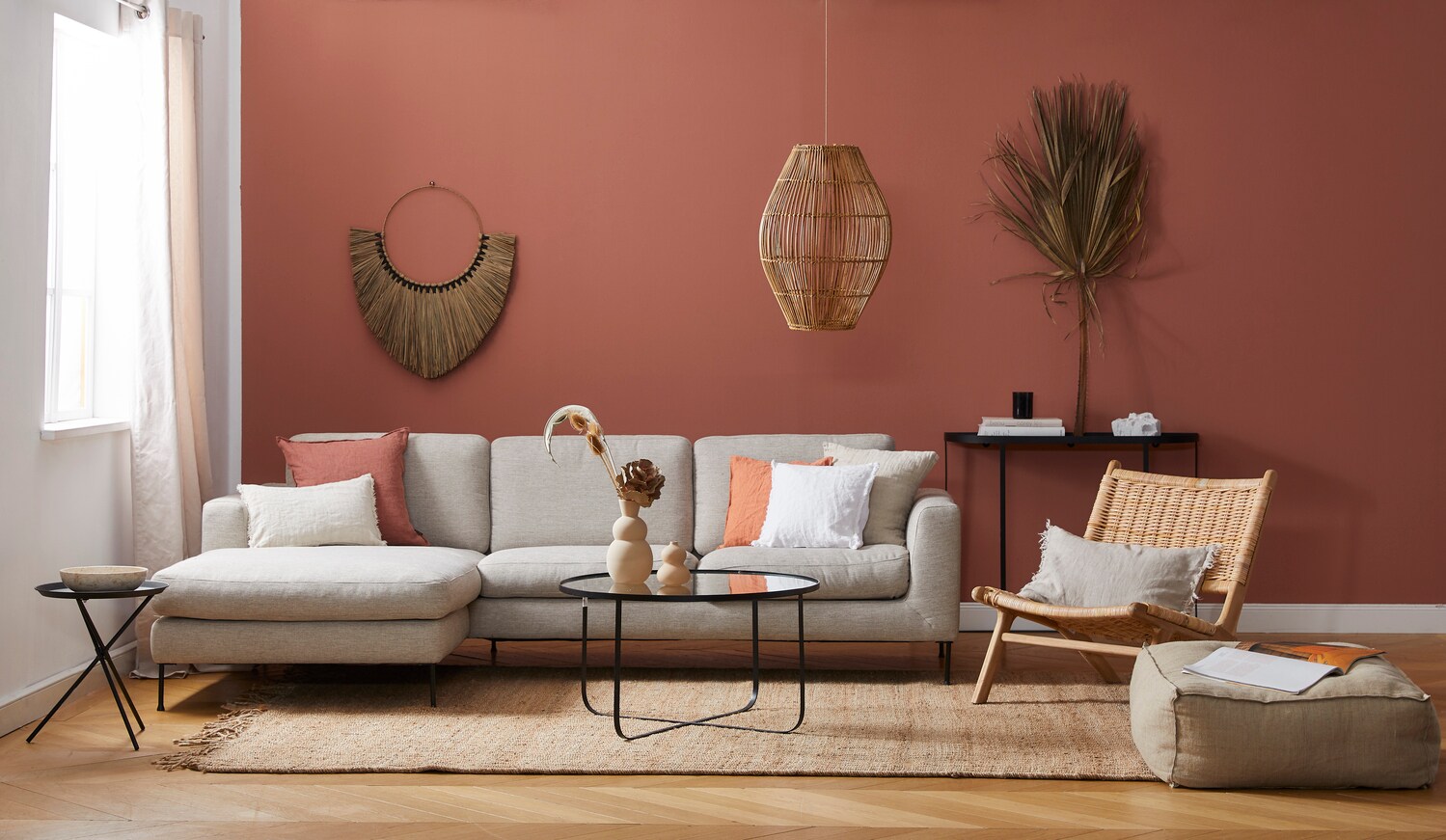 Ein modern eingerichtetes Wohnzimmer mit einem grauen Stoffsofa vor einer terrakottafarbenen Wand Ein modern eingerichtetes Wohnzimmer mit einem grauen Stoffsofa vor einer terrakottafarbenen Wand