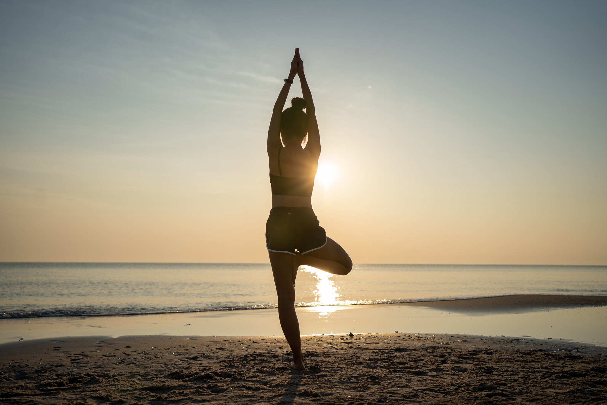 Die Silhouette einer Frau beim Yoga am Strand bei Sonnenuntergang