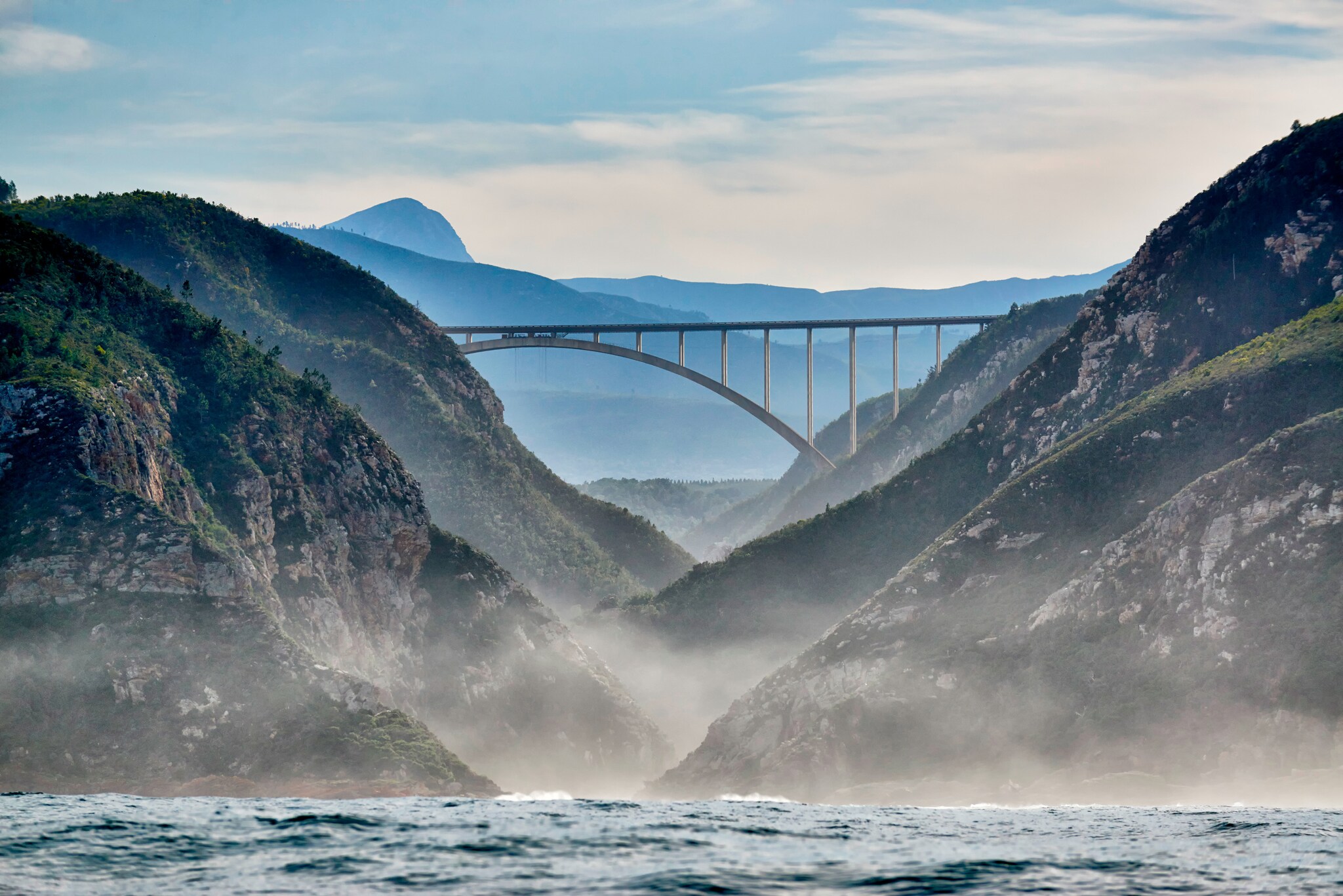 Blick vom Wasser auf eine Brücke, die zwei Berge miteinander verbindet