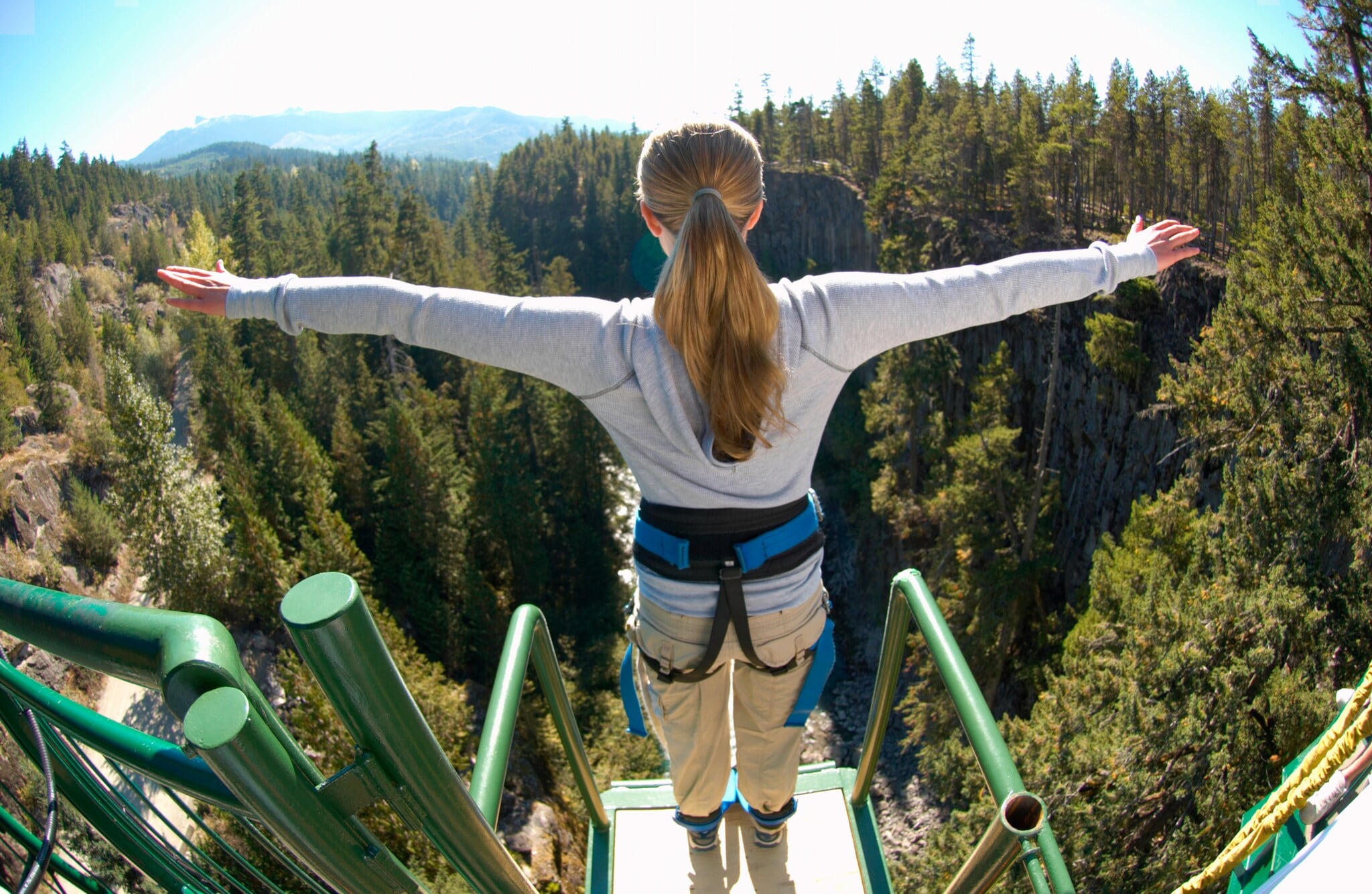 Eine Frau steht mit ausgebreiteten Armen gesichert an einem Bungee-Jumping-Gerüst und ist kurz davor runterzuspringen Eine Frau steht mit ausgebreiteten Armen gesichert an einem Bungee-Jumping-Gerüst und ist kurz davor runterzuspringen