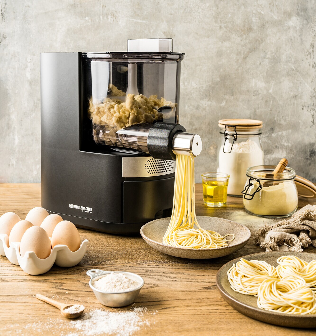 Foto einer elektrischen Nudelmaschine von Rommelsbacher, dekoriert mit Eier, Mehl und Öl.