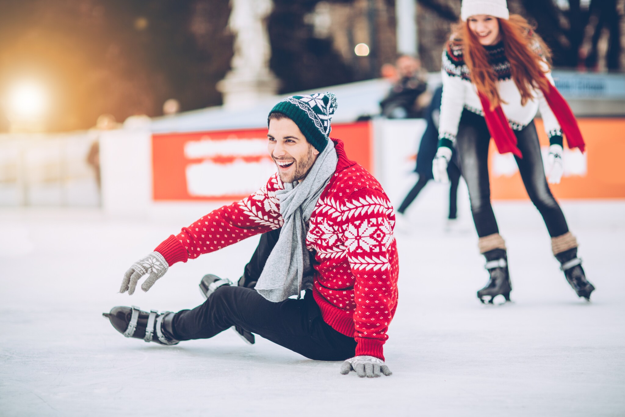 Ein lachendes Paar in weihnachtlicher Kleidung beim Schlittschuhfahren auf einer Eisbahn