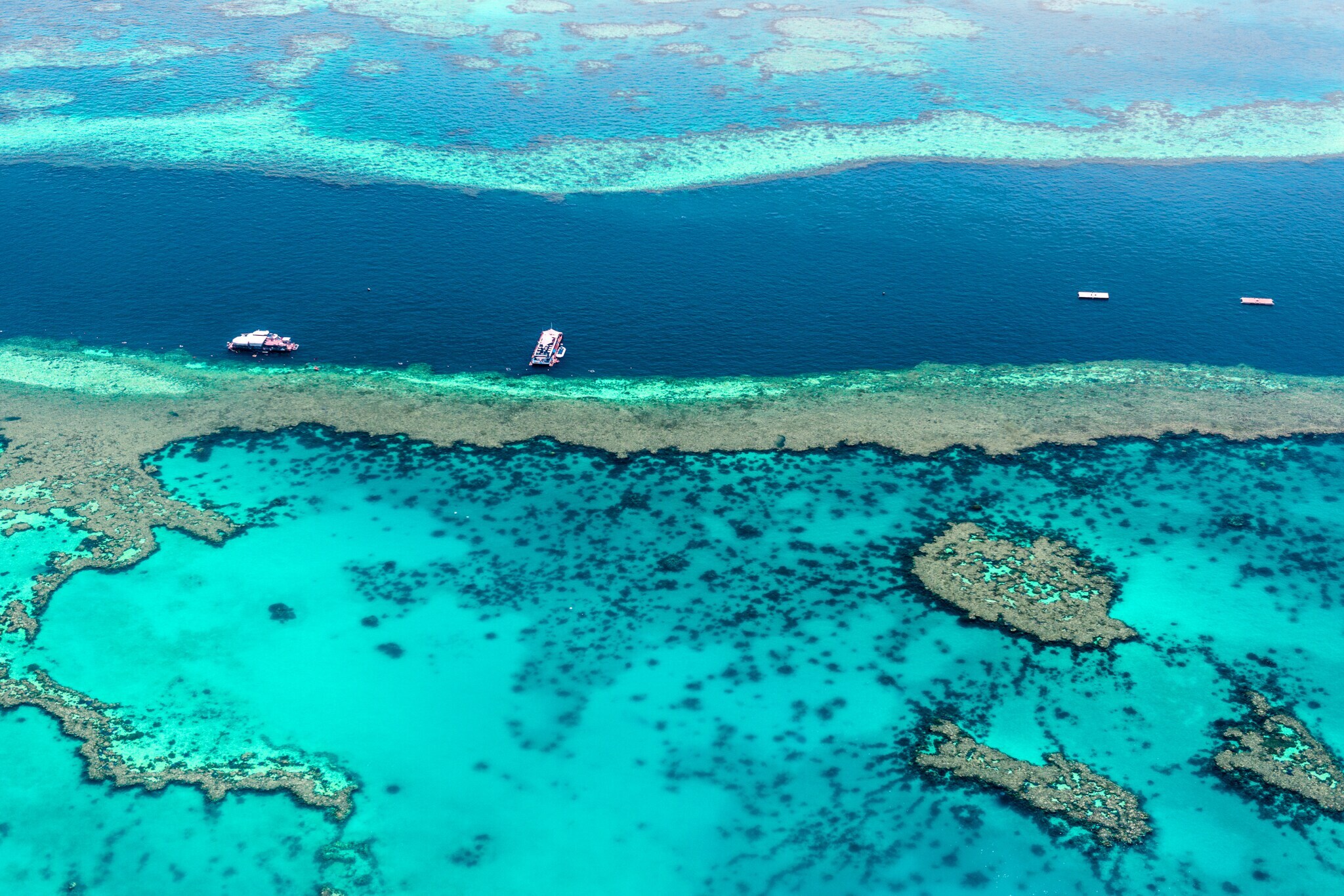 Türkisblaue Wasseroberfläche des Great Barrier Reef mit Booten aus der Luft