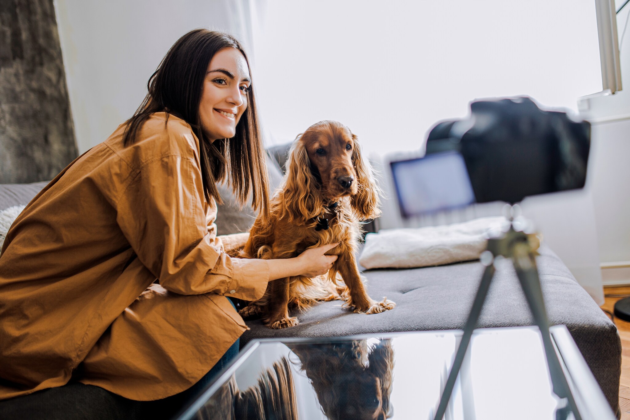Eine junge Frau posiert mit Hund vor einer Kamera auf einem Stativ.