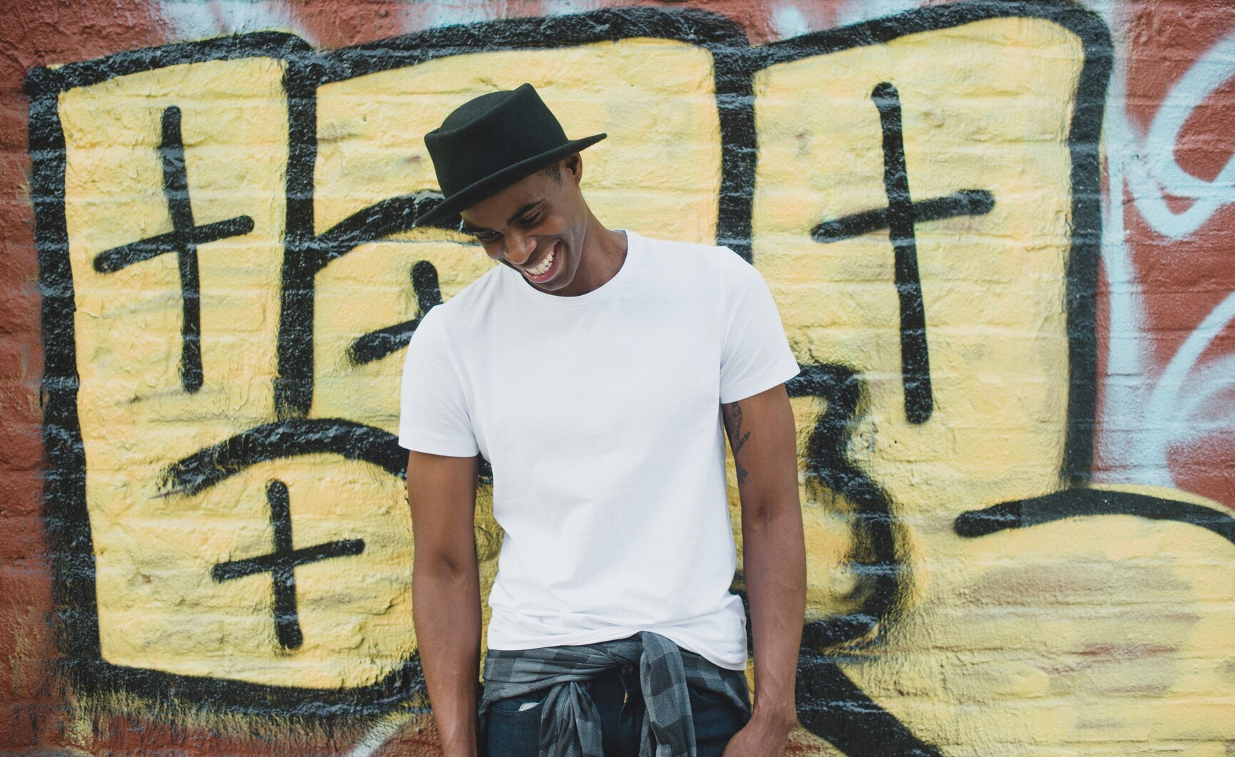 Ein junger Mann mit Hut in einem weißen T-Shirt vor einer Grafittiwand